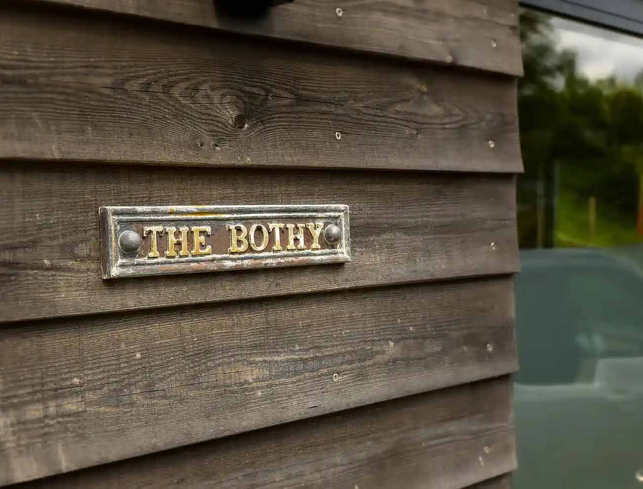 Close-up of “The Bothy” metal sign on weathered timber cladding.