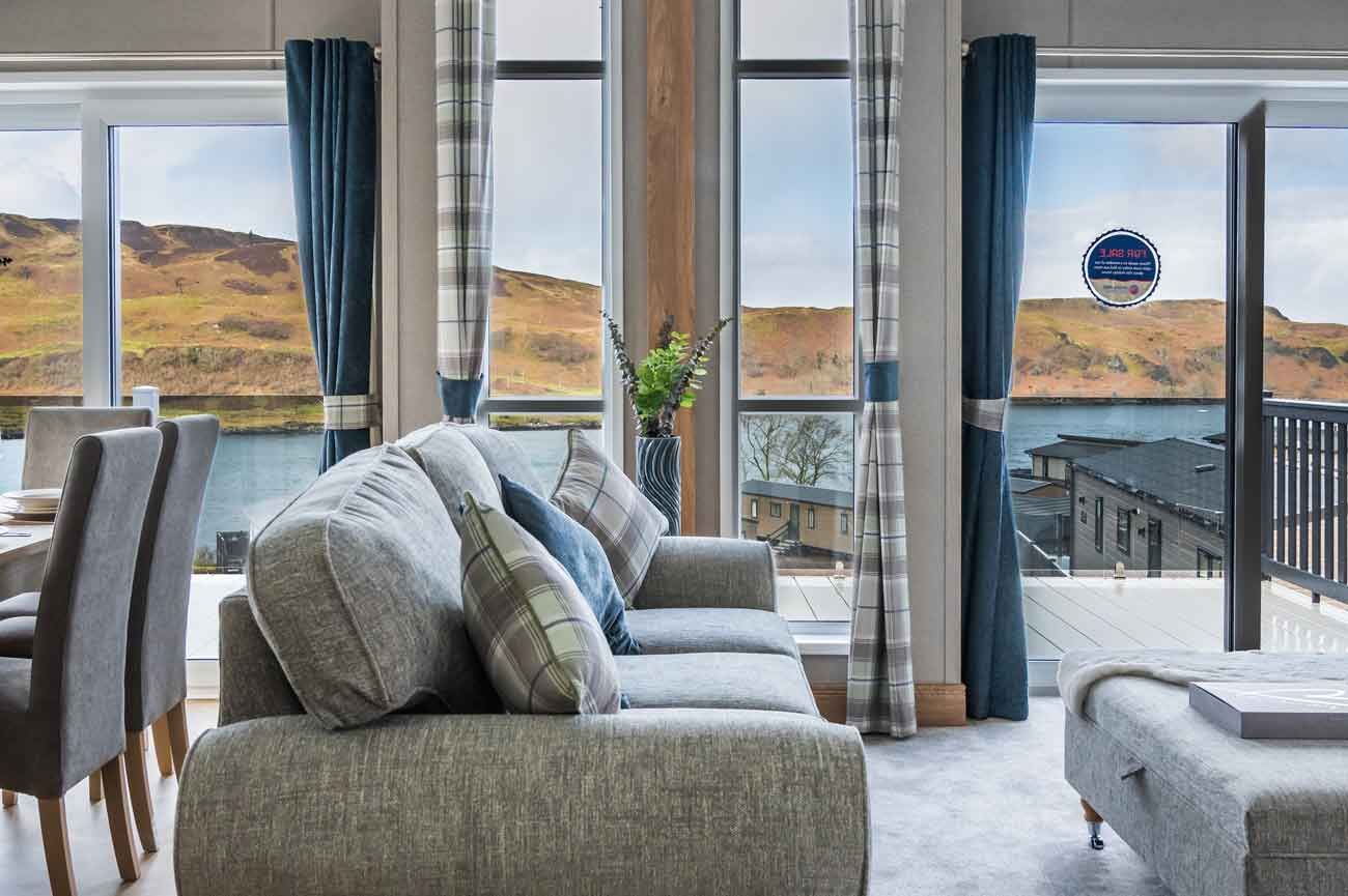 A modern grey sofa in a bright living space with large glass doors opening up to an expansive water and hill view.