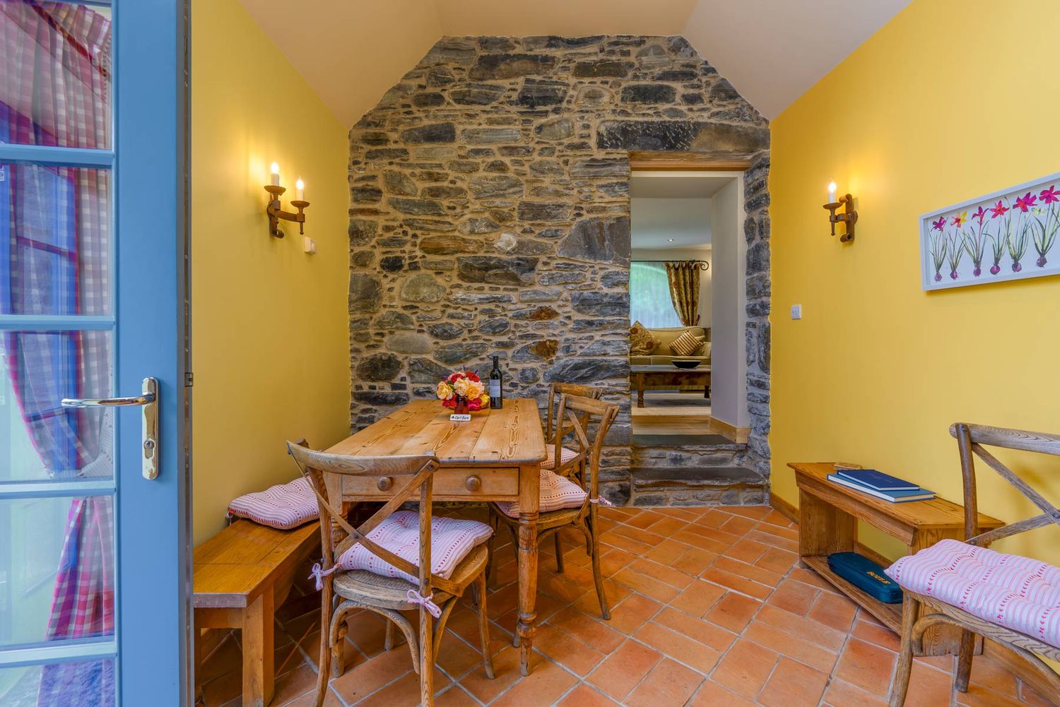 Rustic dining area with yellow walls, stone accent wall, wooden table, and blue double doors.