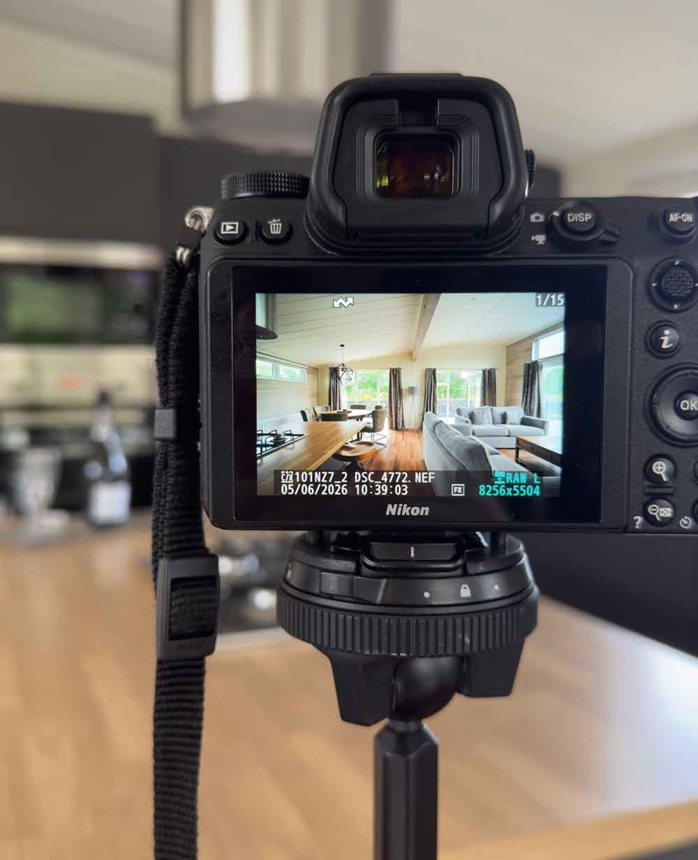 A close-up of a professional camera on a tripod, showing an interior room shot on its digital live view screen.