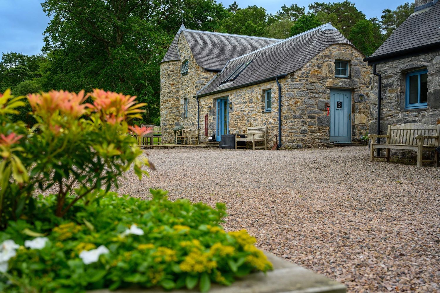 Traditional Scottish stone cottage with blue wooden doors and gravel courtyard surrounded by lush greenery