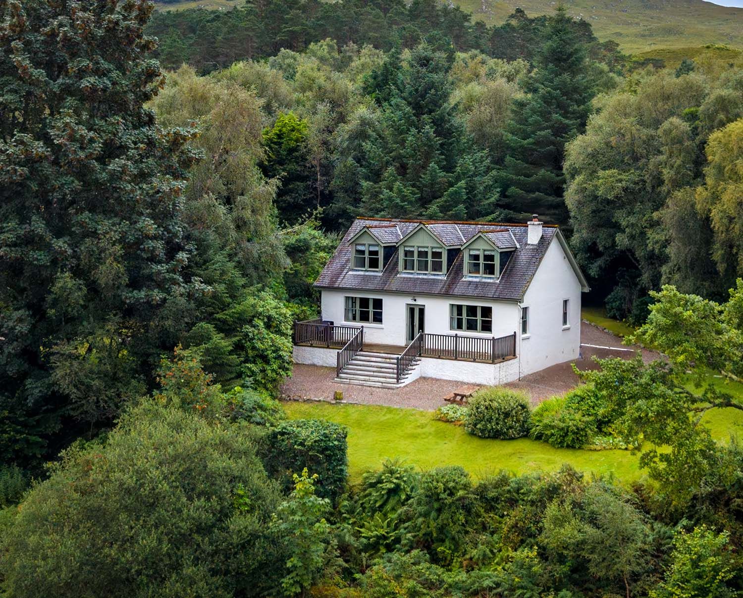 Drone photograph of a traditional white Highland cottage surrounded by woodland and countryside.