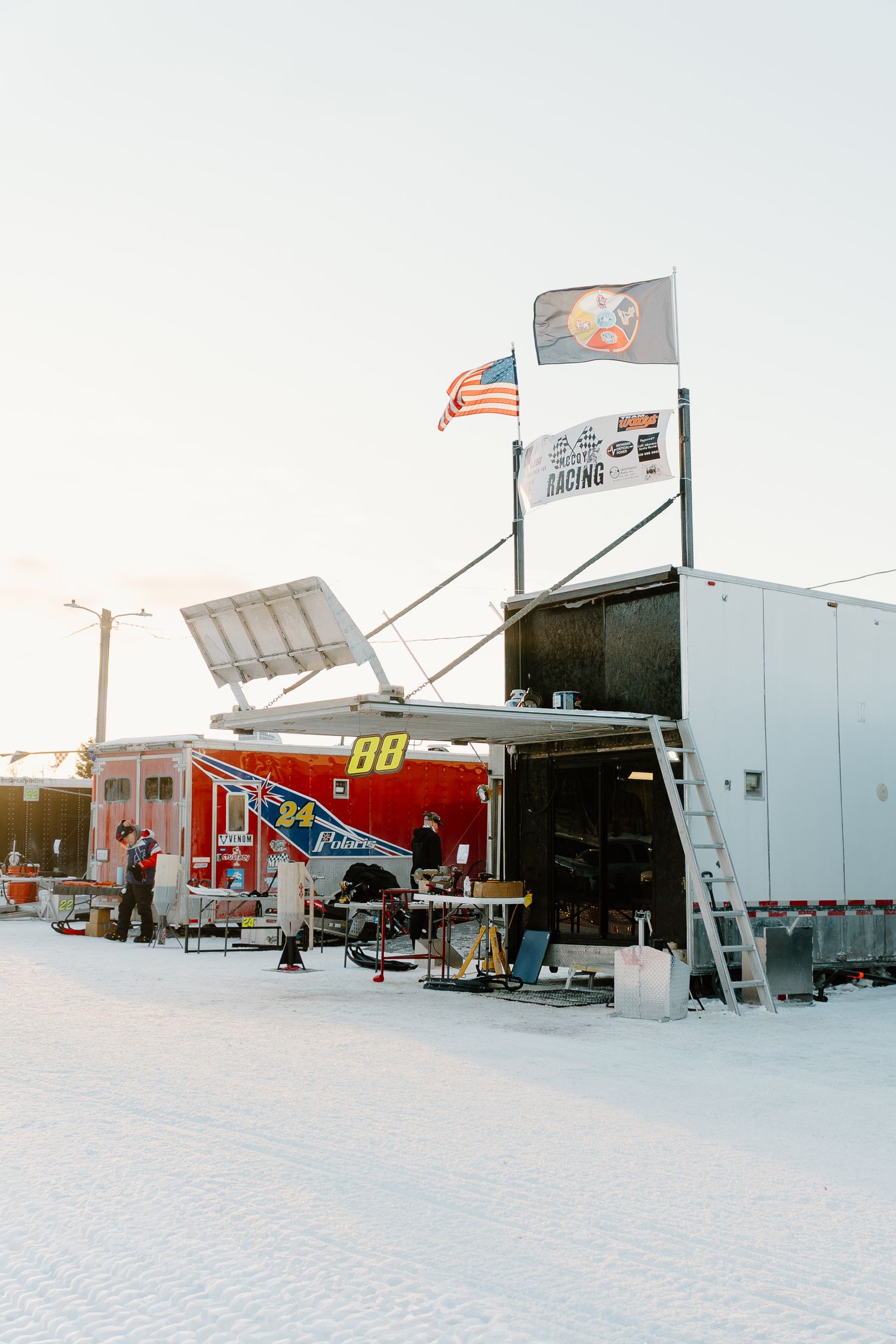 Race team trailer numbered 88 with American flag and racing flags displayed at a winter snowmobile event.