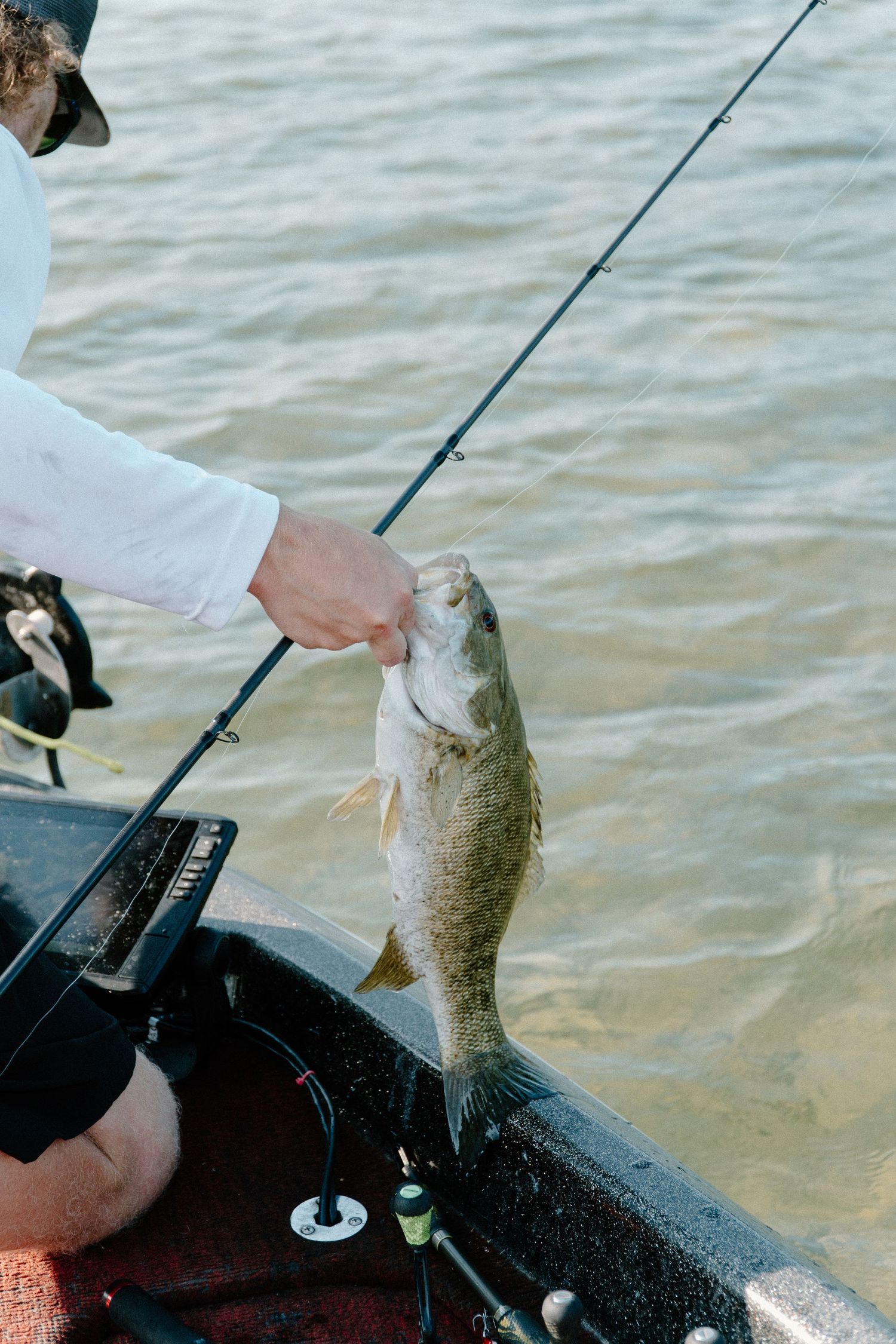 Fisherman holding a largemouth bass caught while fishing from a boat on a lake.