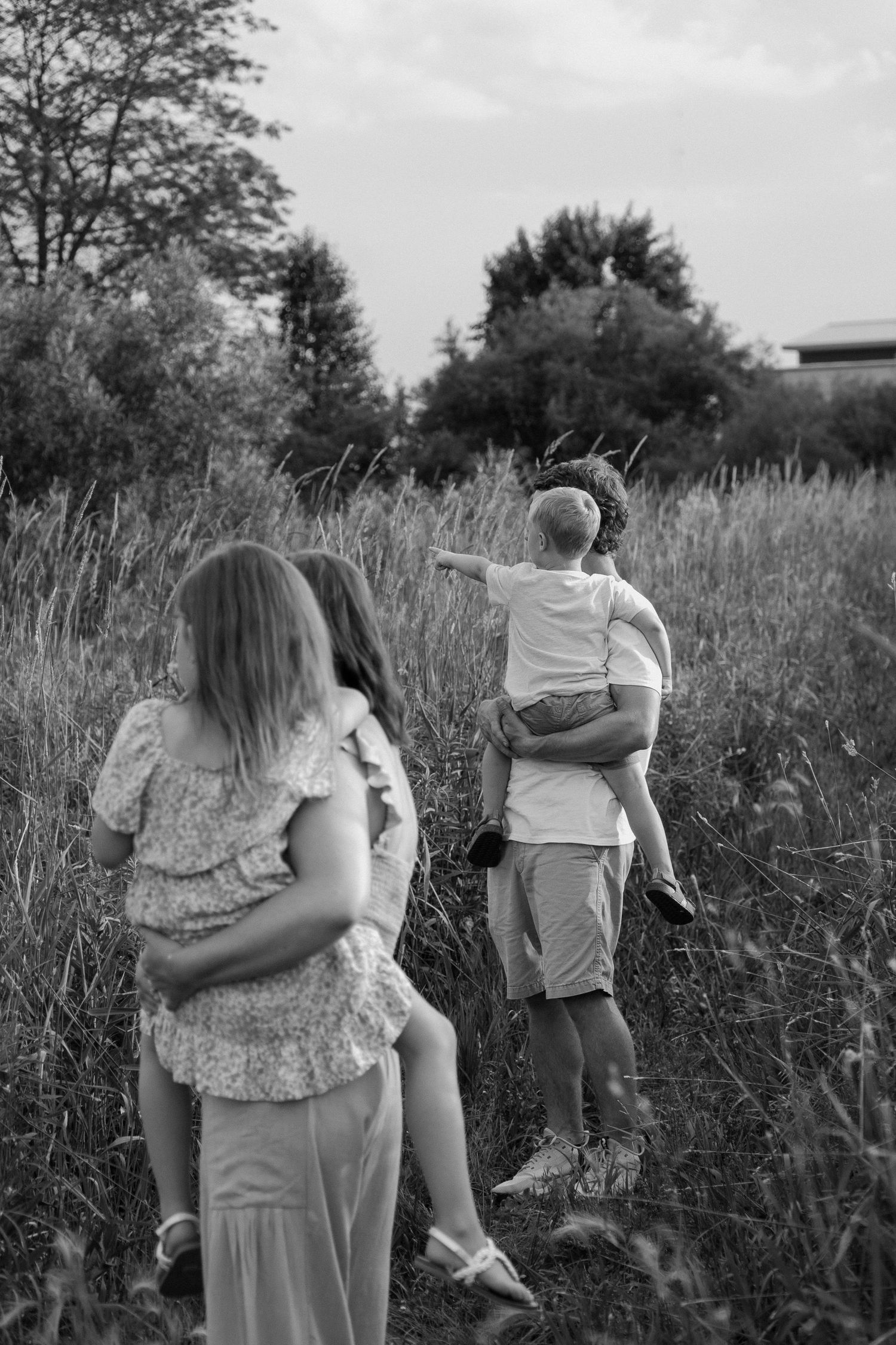 Black and white photo of family walking through tall grass field with father carrying child.