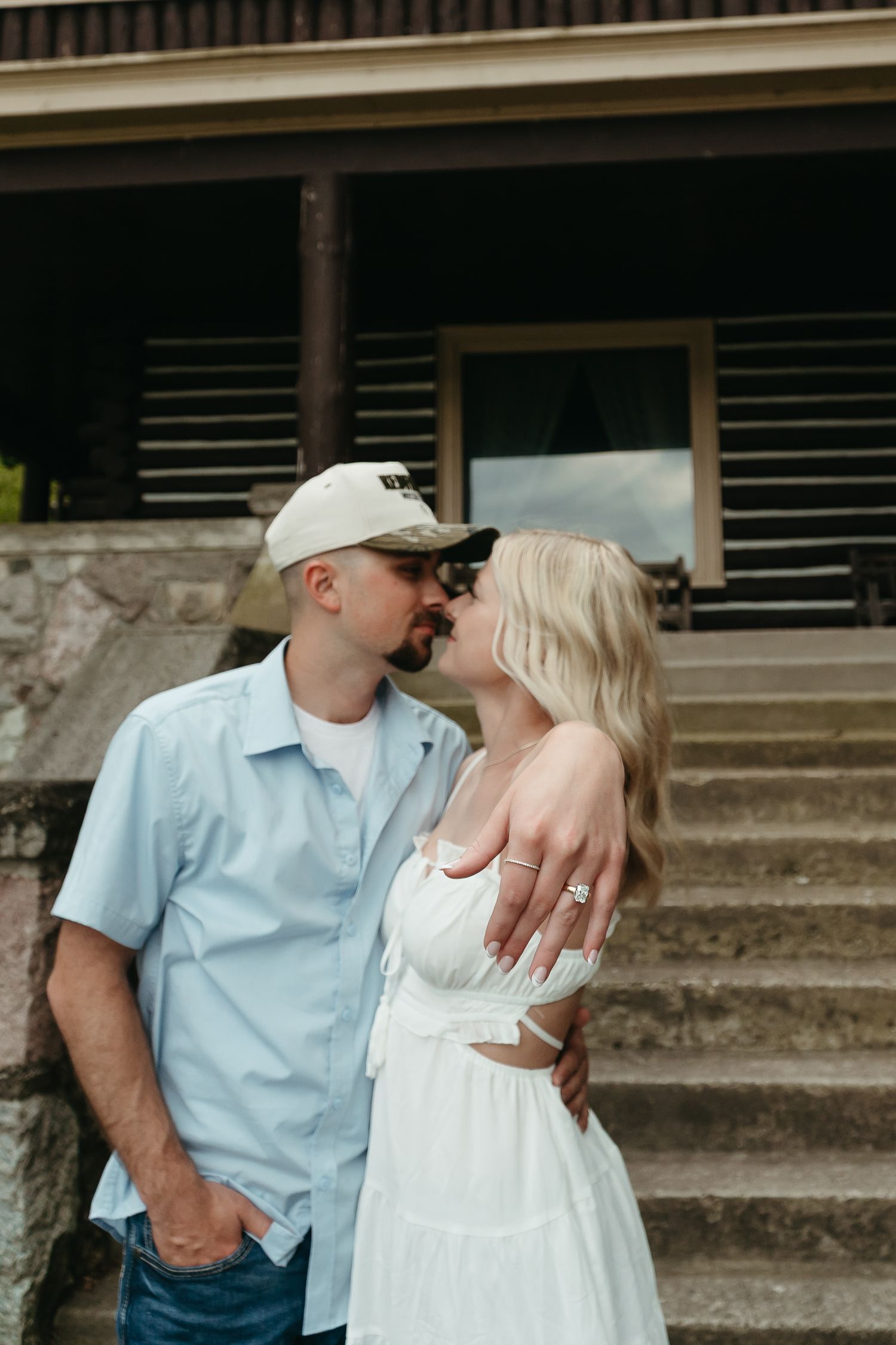 Couple sharing a kiss on stone steps, man in blue shirt and cap, woman in white dress.
