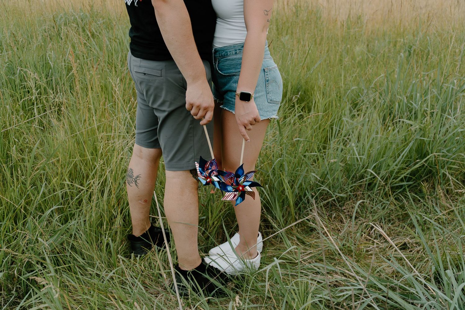 Couple holding a patriotic pinwheel while standing together in a tall grass field.
