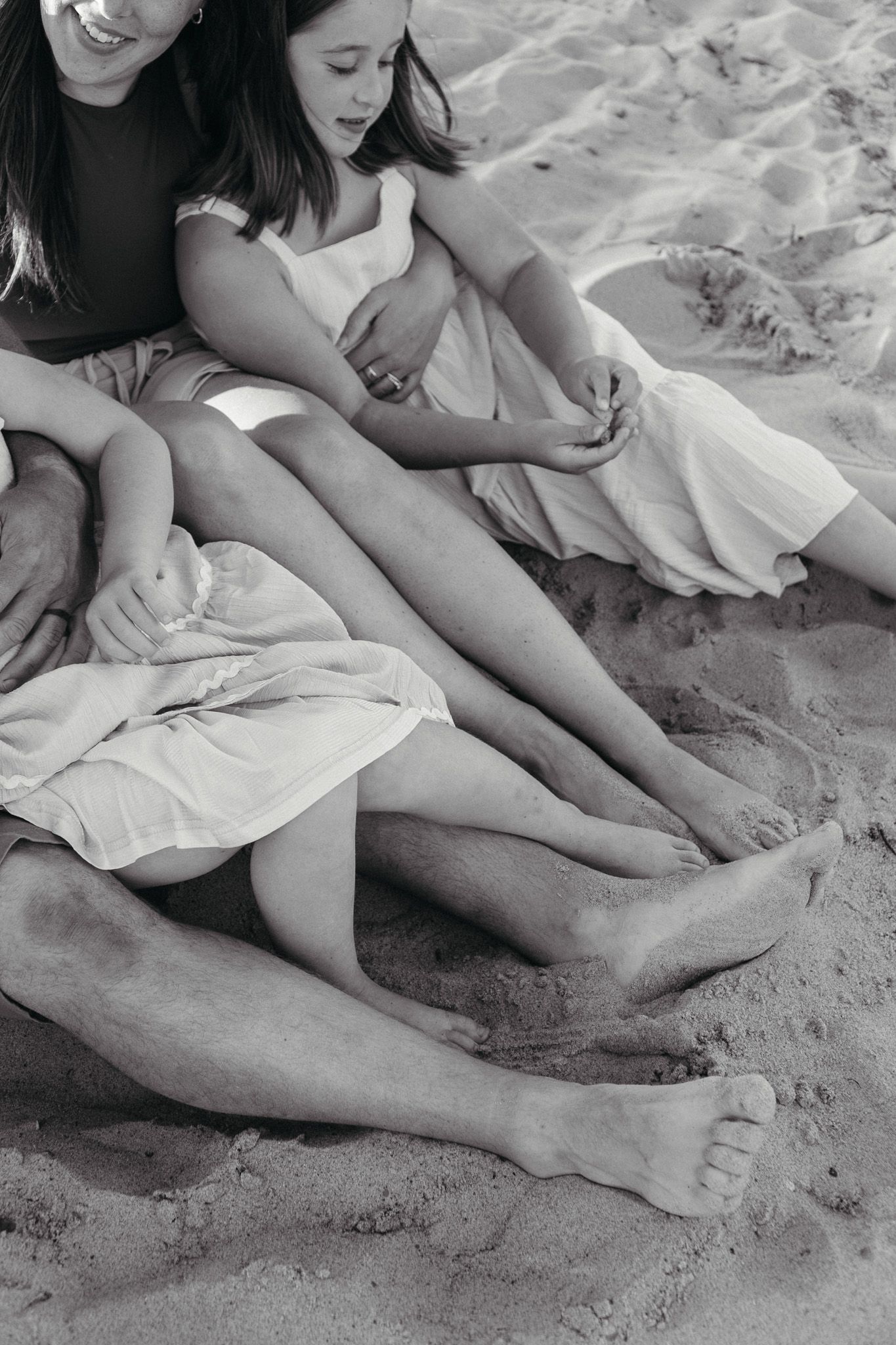 Black and white photo of a family sitting barefoot together on a sandy beach.