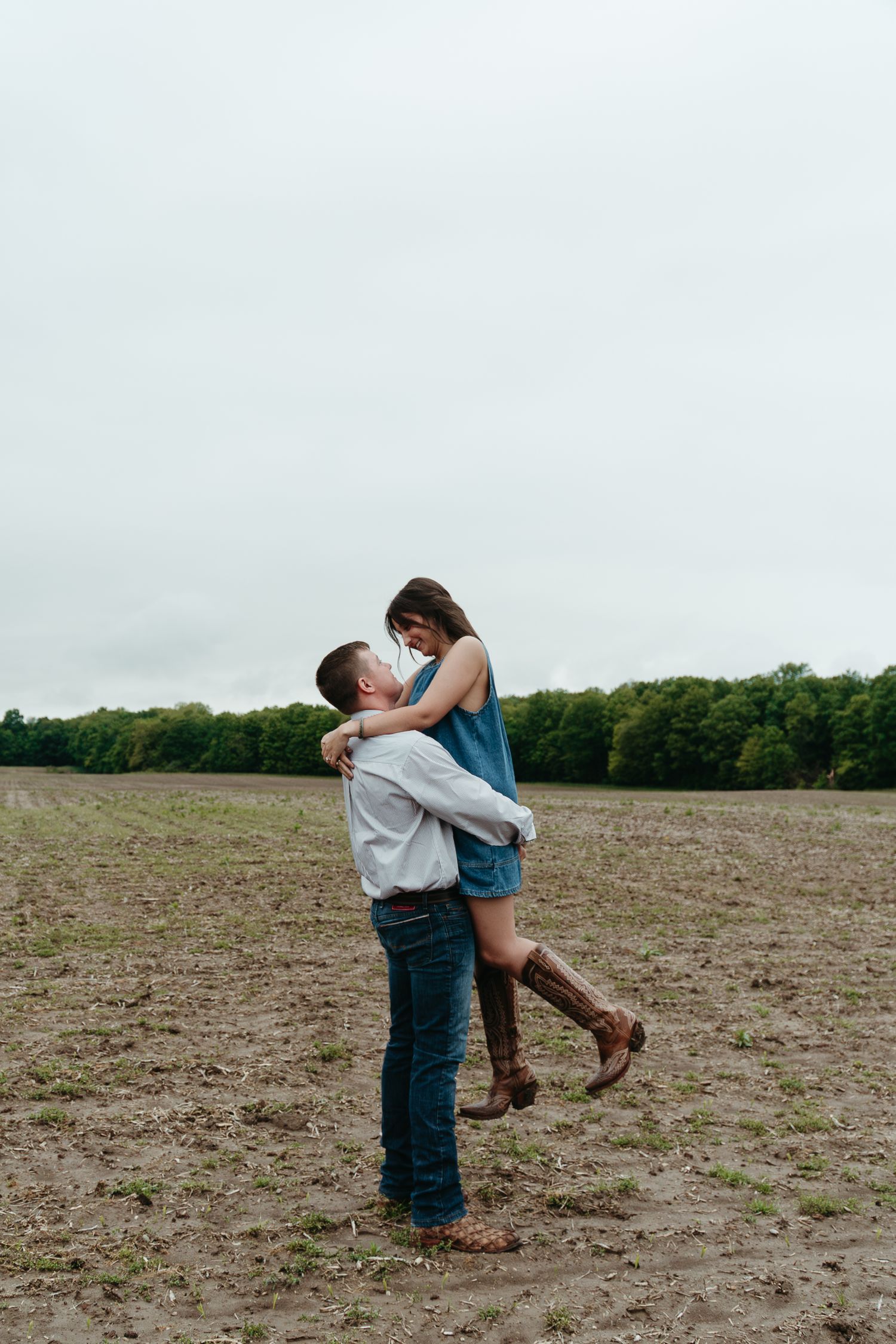 Man lifting woman in romantic embrace in an open muddy field with treeline in the background.