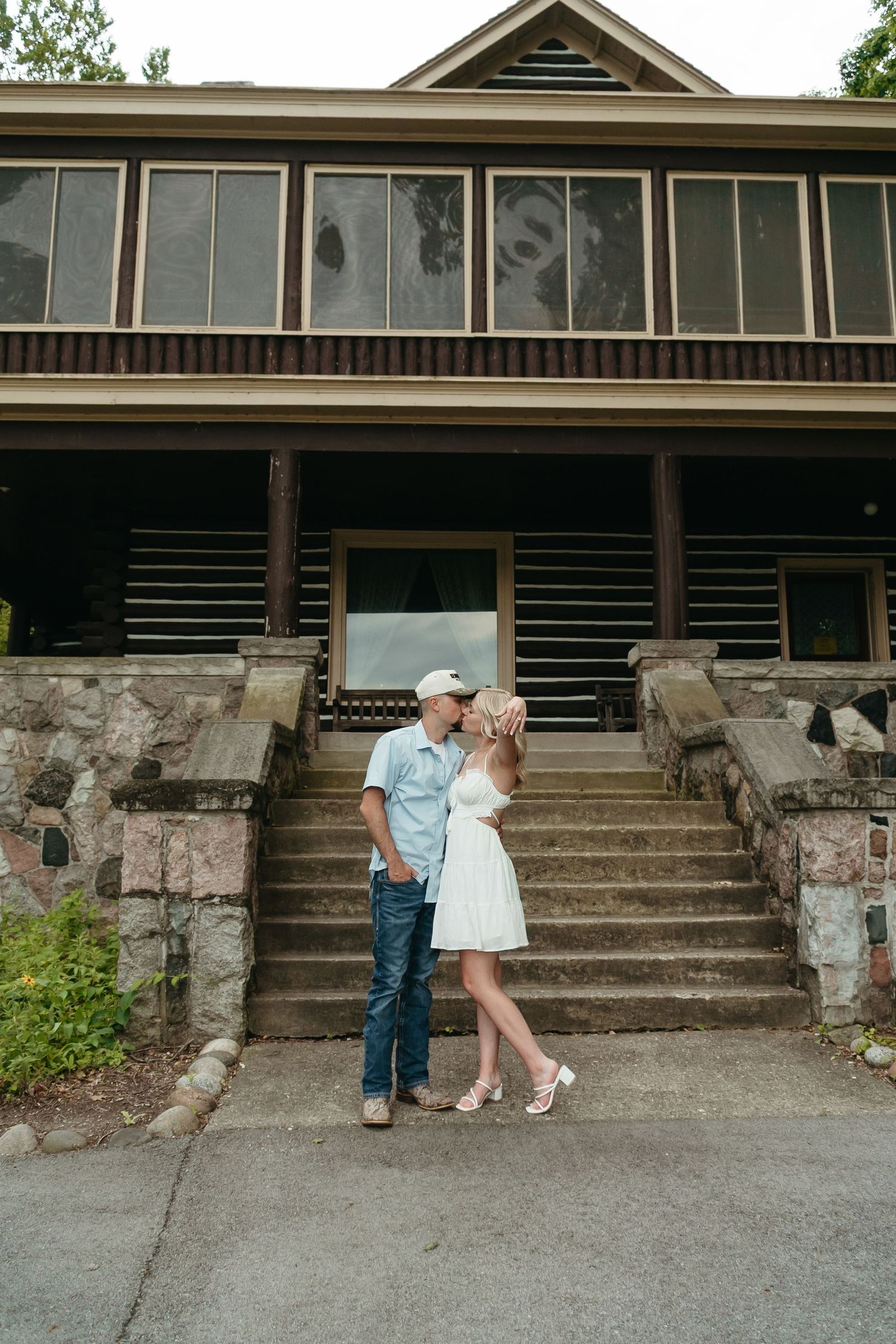 Couple kissing in front of a rustic log cabin with stone steps.