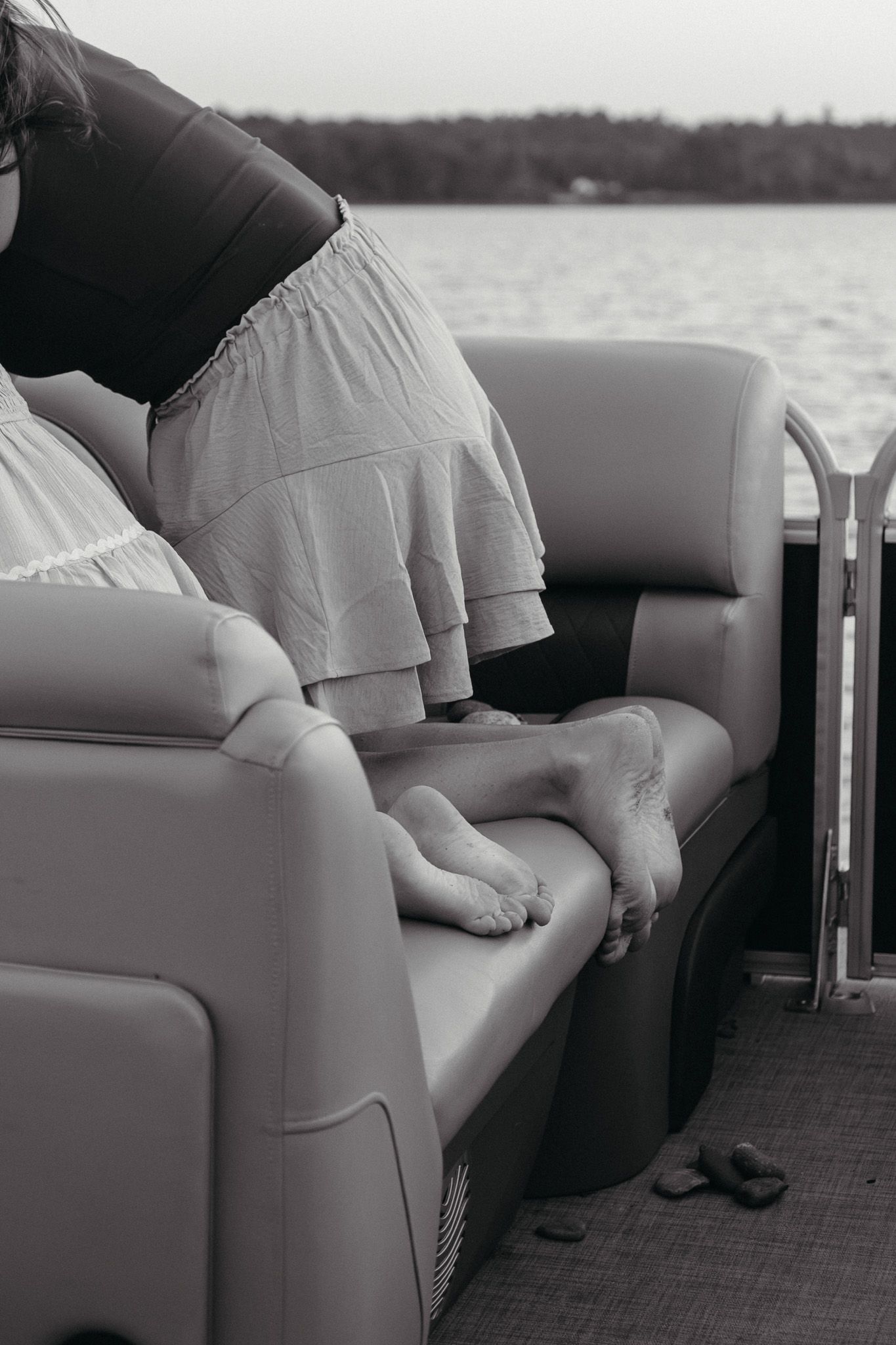Black and white photo of children resting barefoot on cushioned pontoon boat seats near open water.