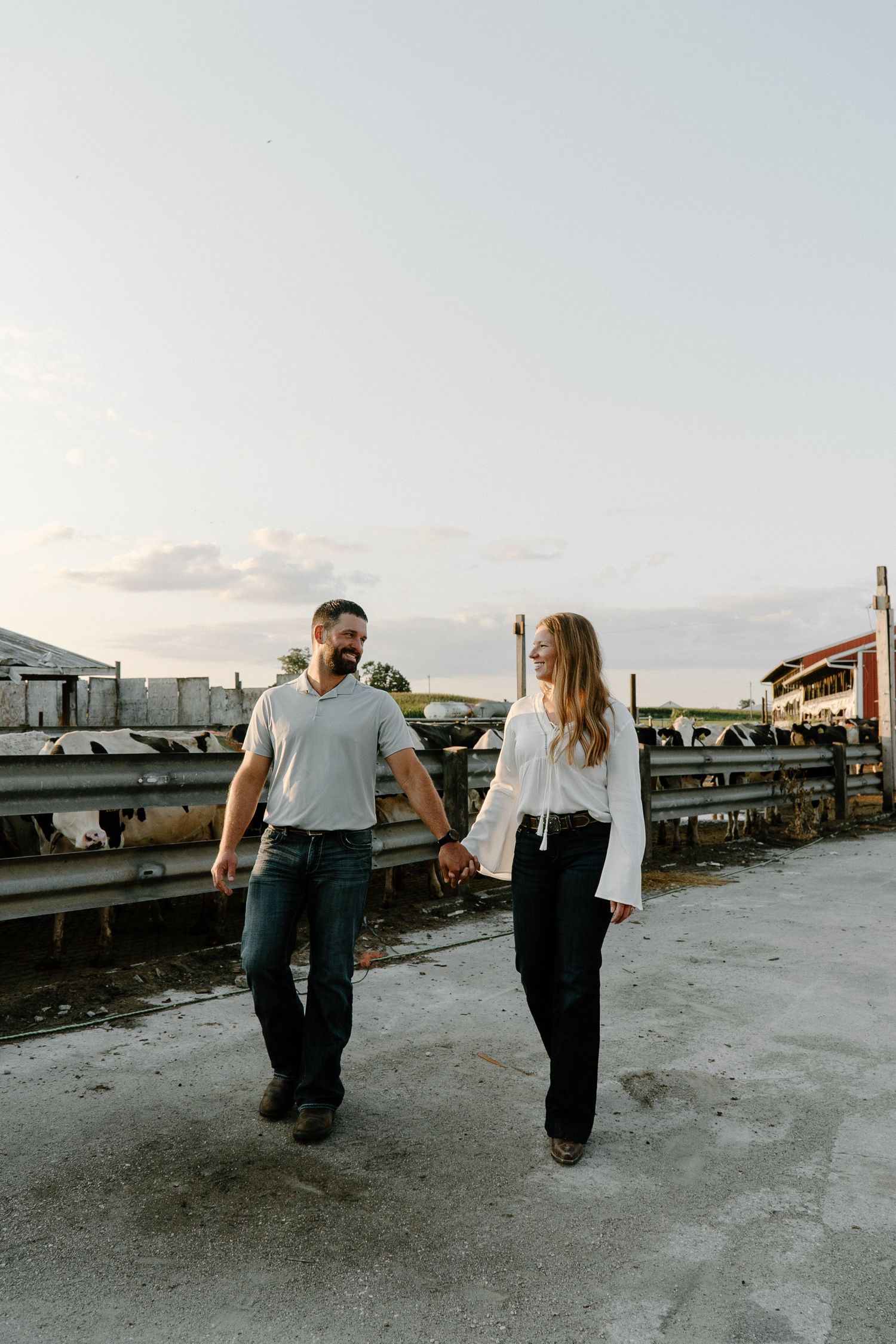 Smiling couple holding hands while walking at dairy farm during sunset.