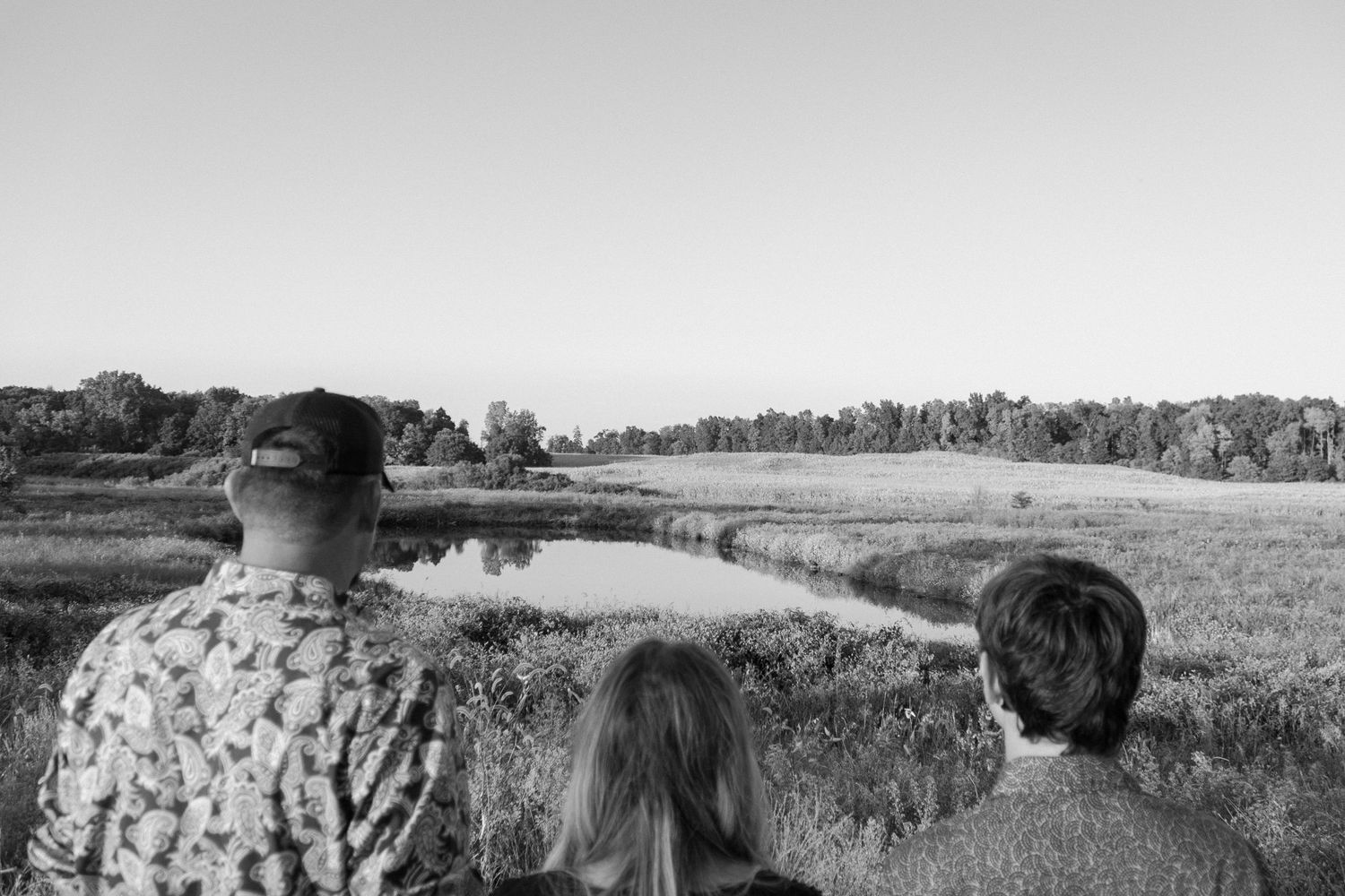 Black and white photo of family looking over peaceful pond in field.