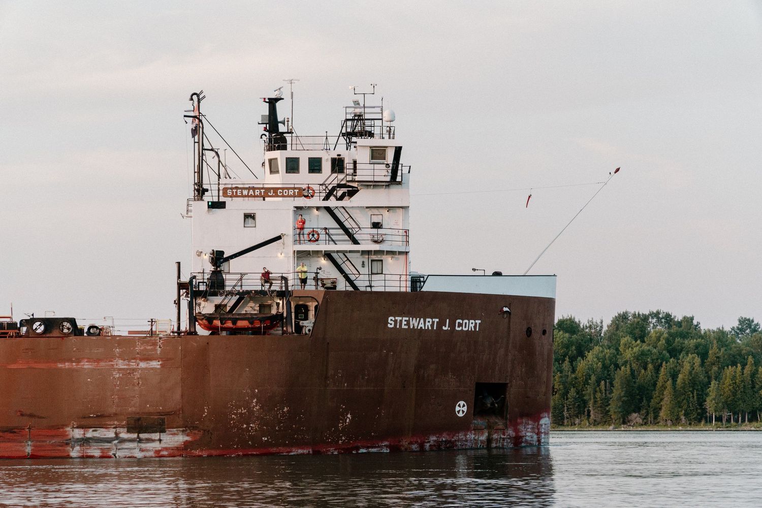 Stewart J. Cort bulk carrier cargo ship navigating a river near a tree-lined shore.