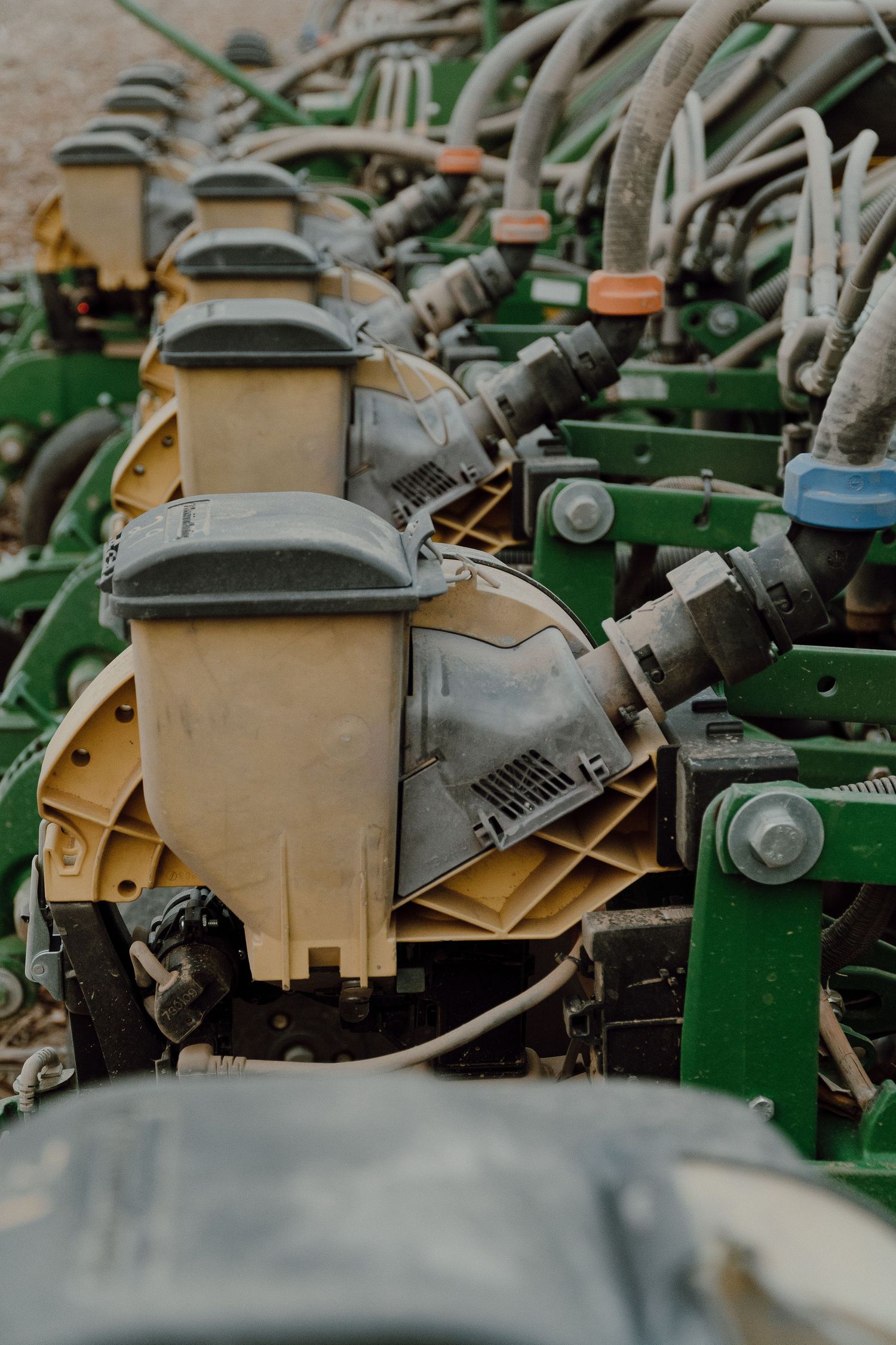 Row of yellow seed meters on a green John Deere corn planter with hydraulic lines.