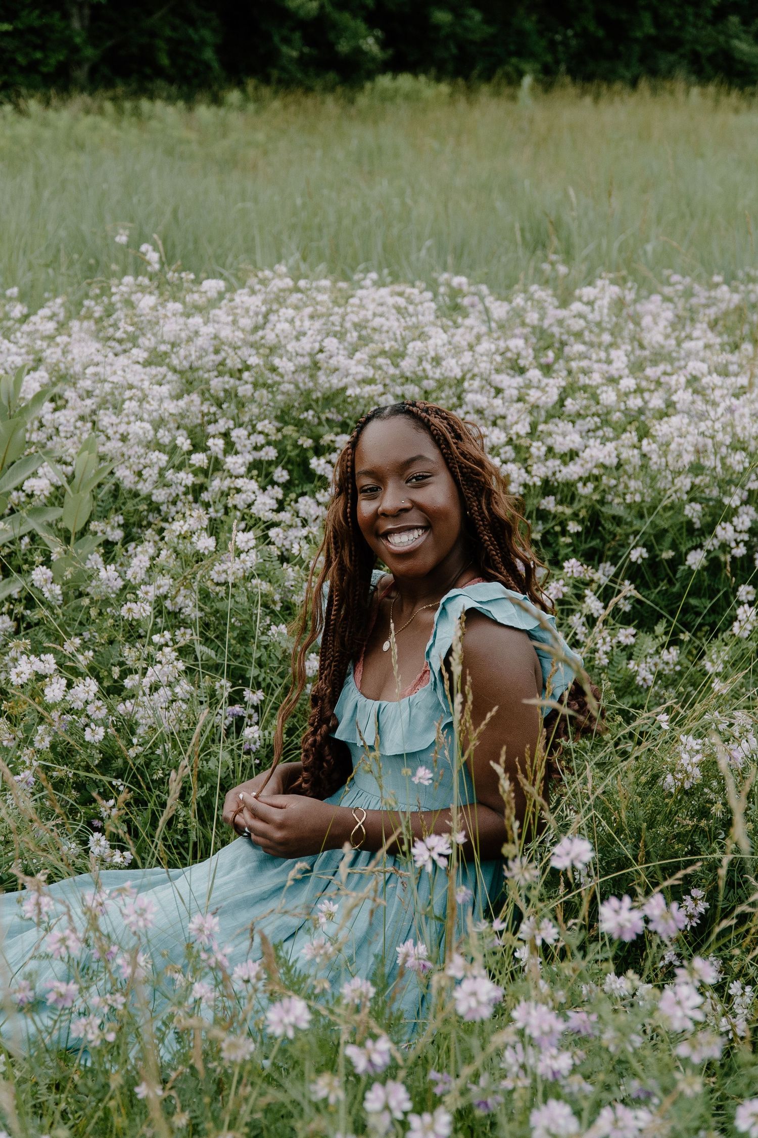 Smiling young Black woman in teal dress sitting in a wildflower meadow with pink blooms.