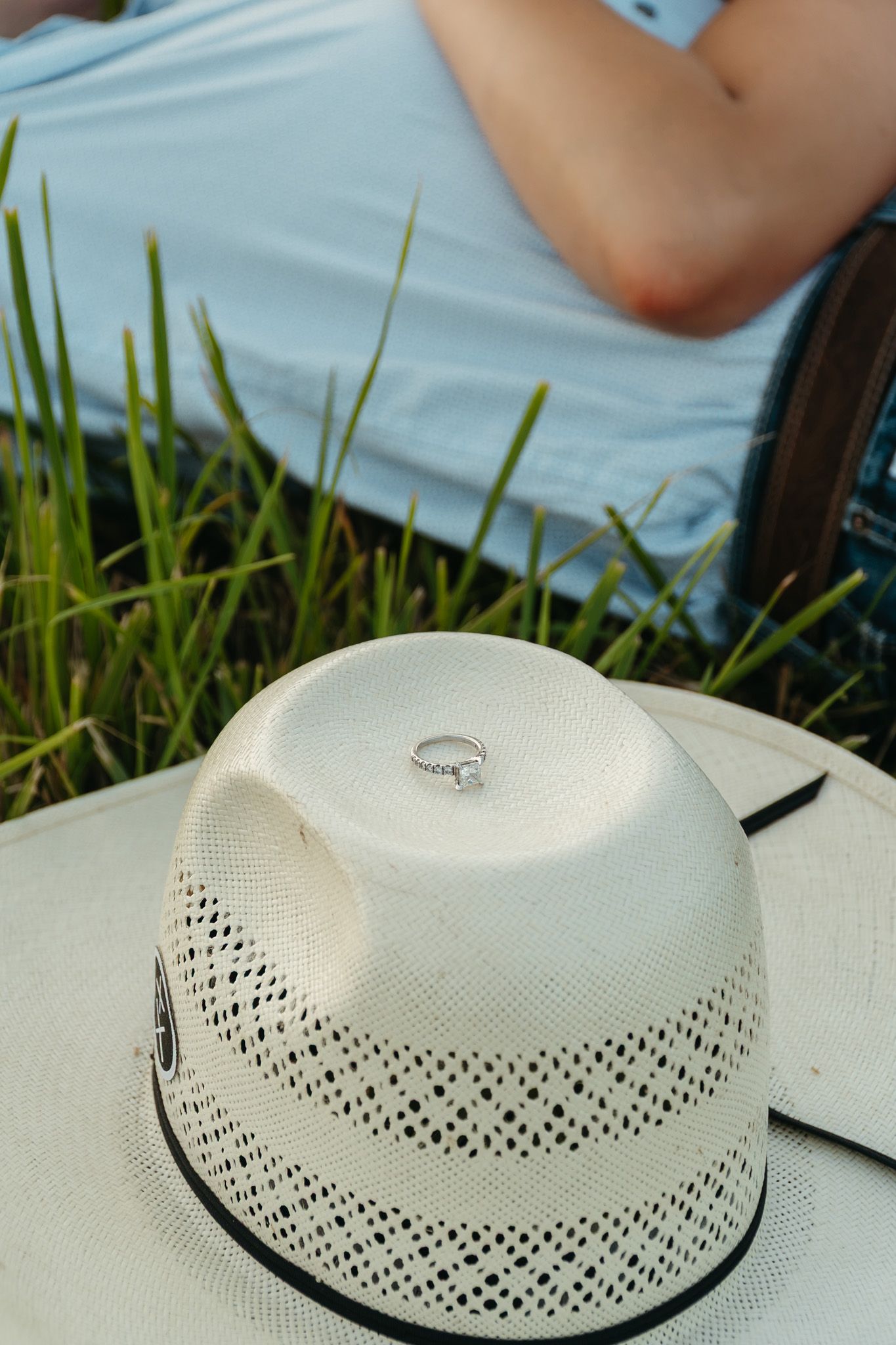 Diamond engagement ring resting inside a white cowboy hat on green grass.