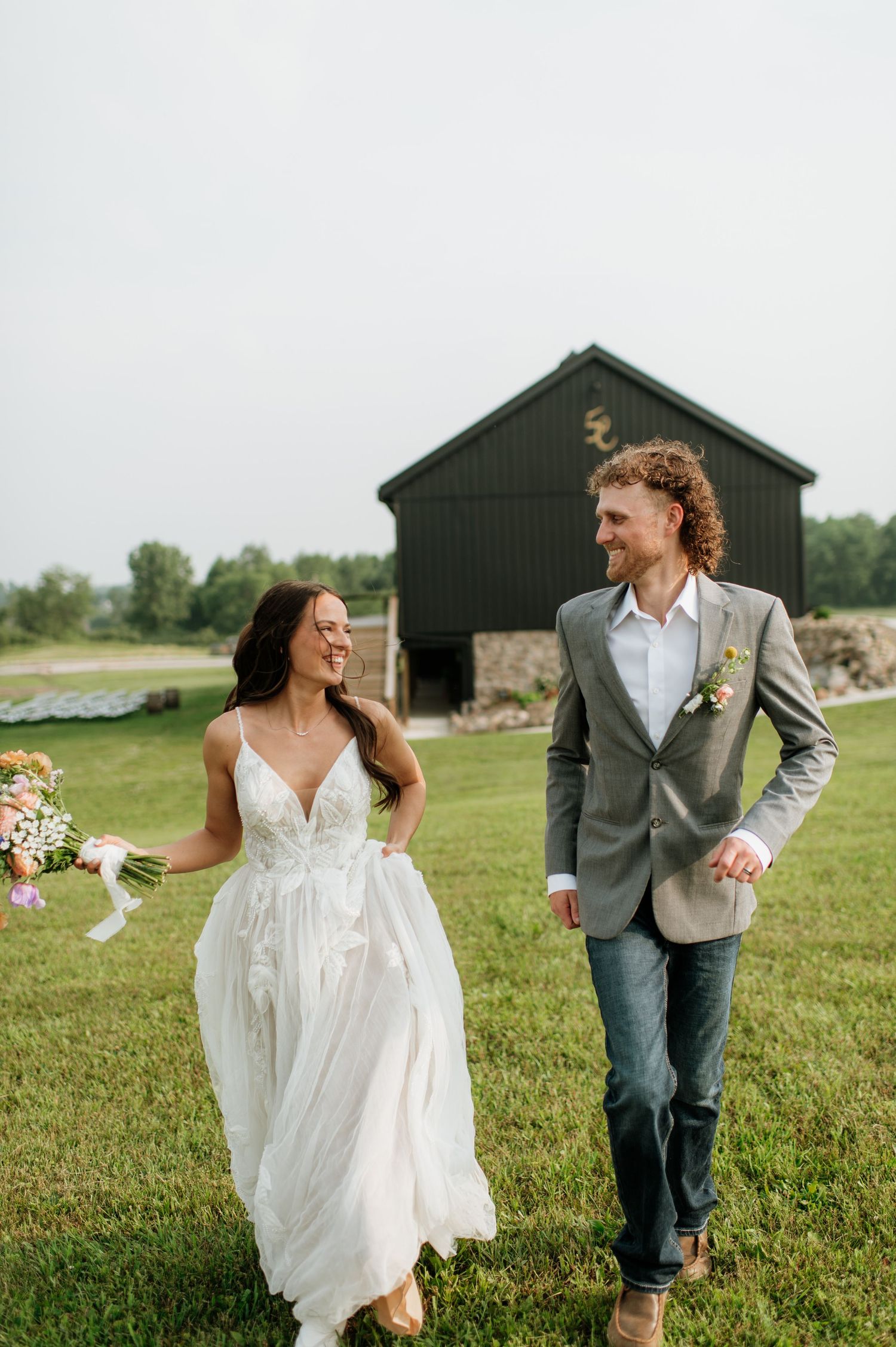 Bride and groom walking together in front of a dark barn on their wedding day.