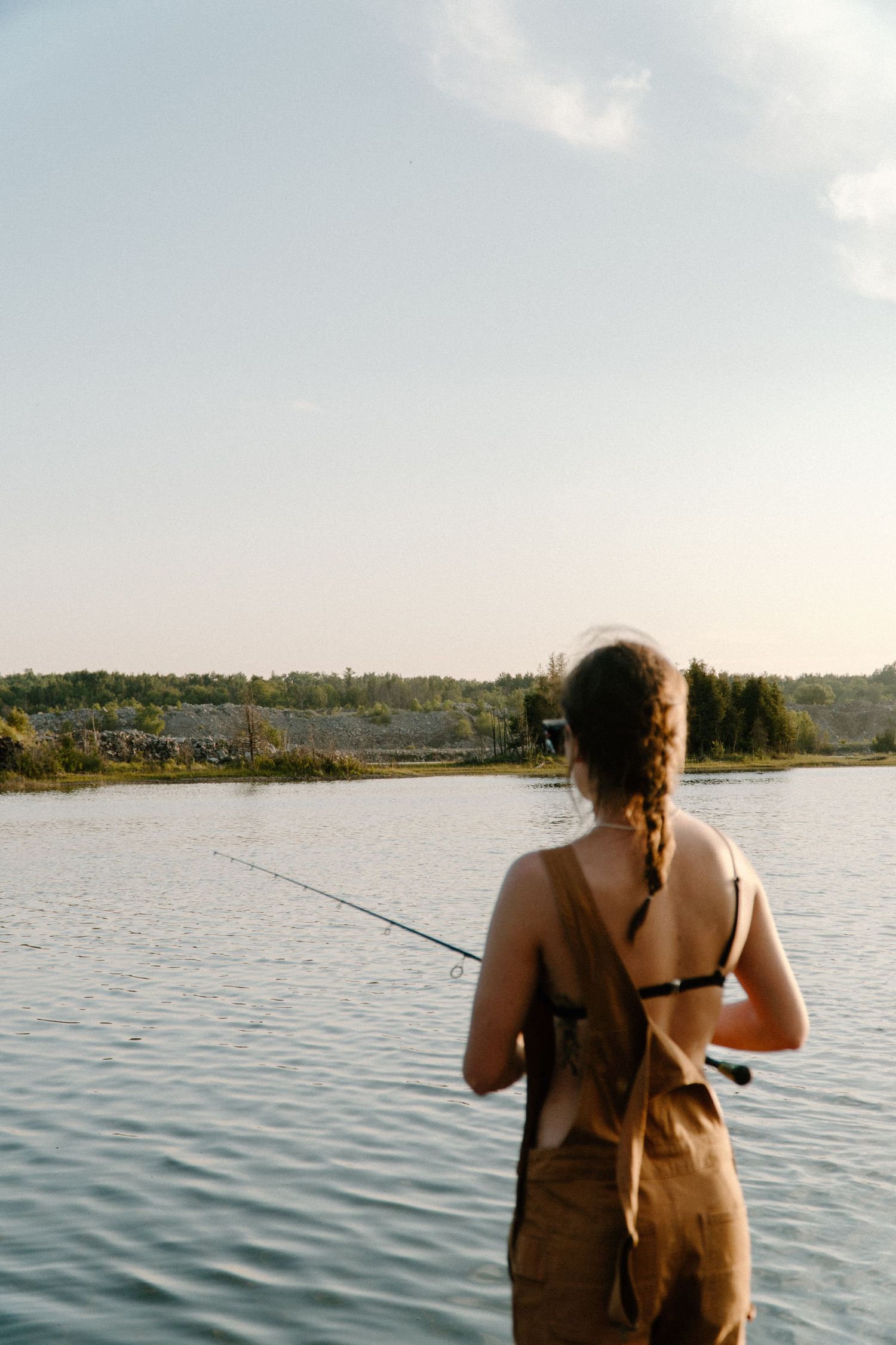 Young woman with braided hair fishing in a calm lake at golden hour.