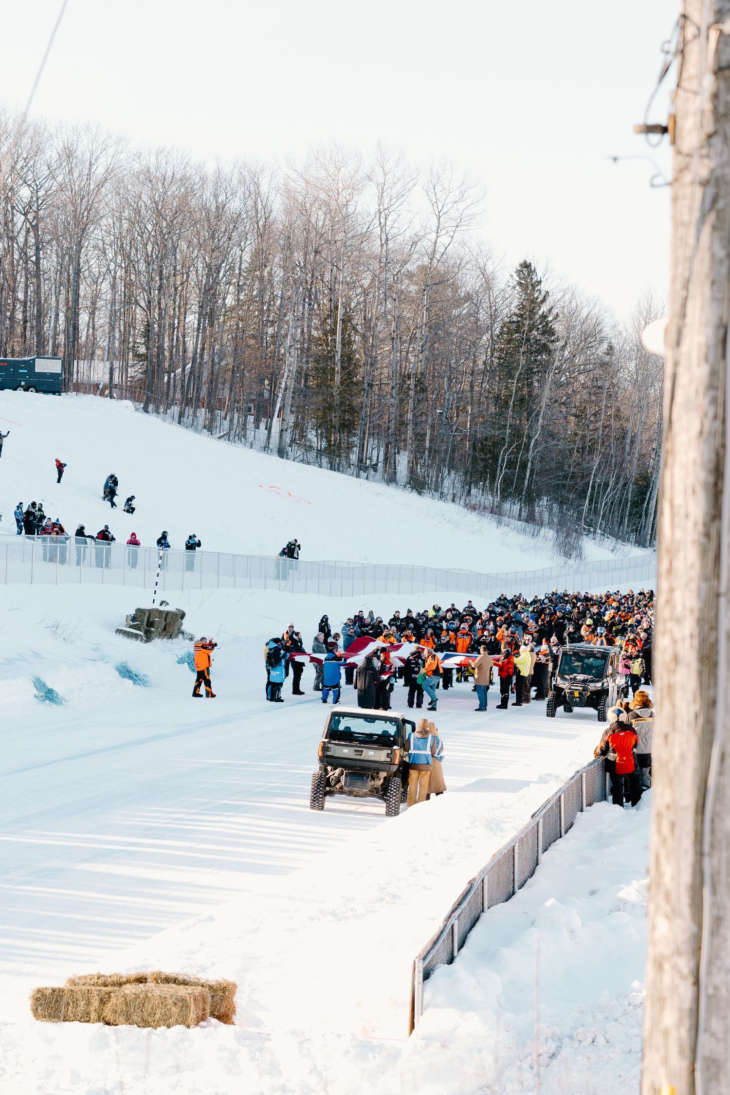 Crowd of spectators lining a snowy race track watching an off-road vehicle competition at a winter motorsport event.