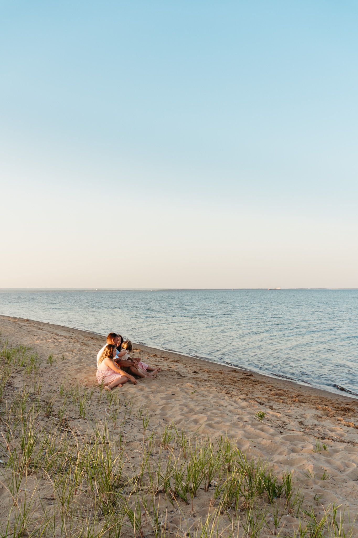 Mother and young child sitting together on sandy beach at sunset near calm ocean waters.