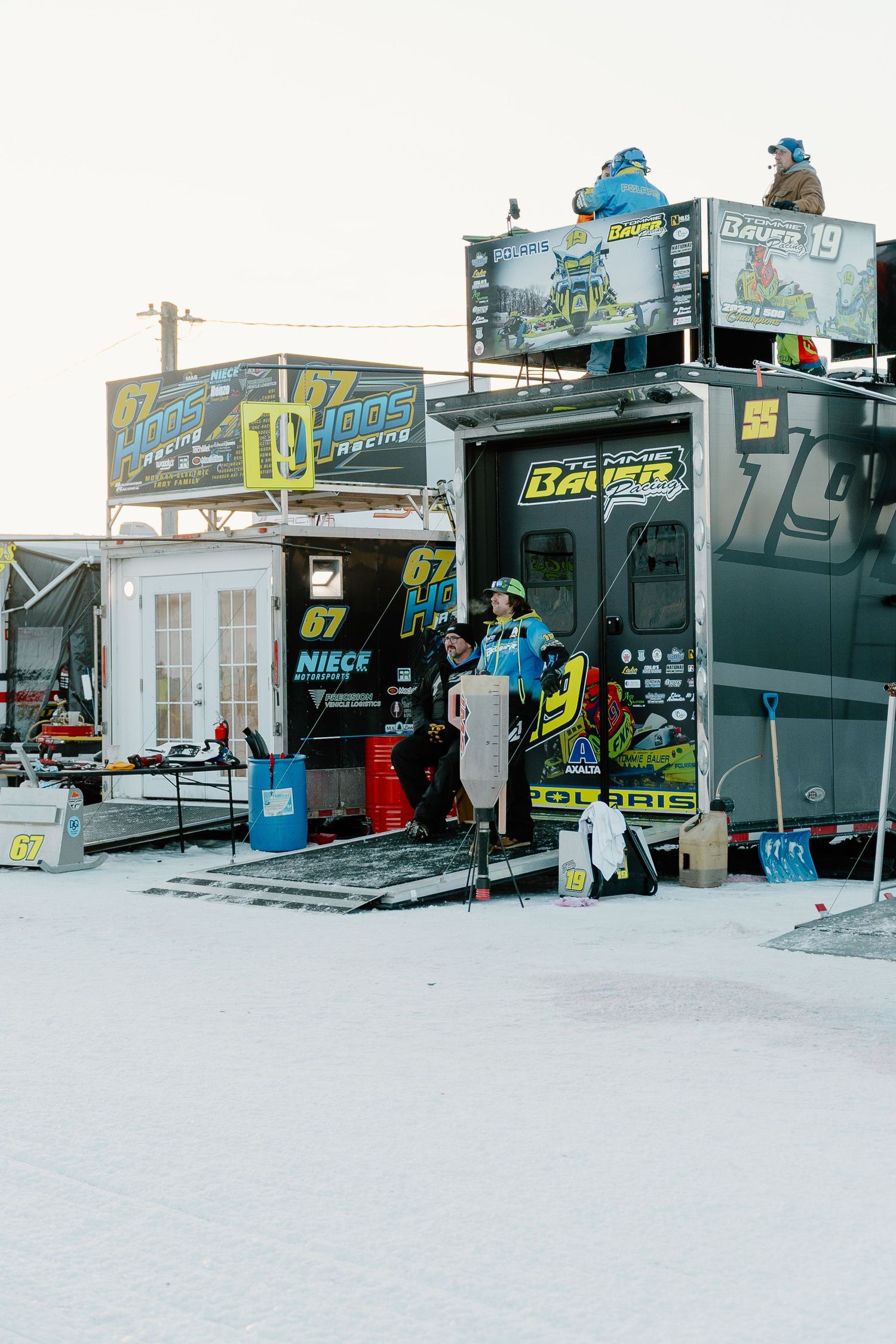 Racing team trailers with Bauer and Jonas Racing branding set up at a winter snowmobile racing event.