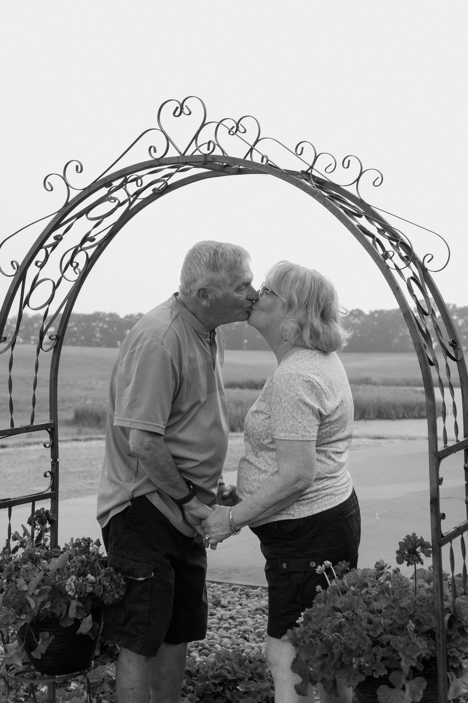 Black and white photo of an older couple kissing under a decorative iron garden arch.
