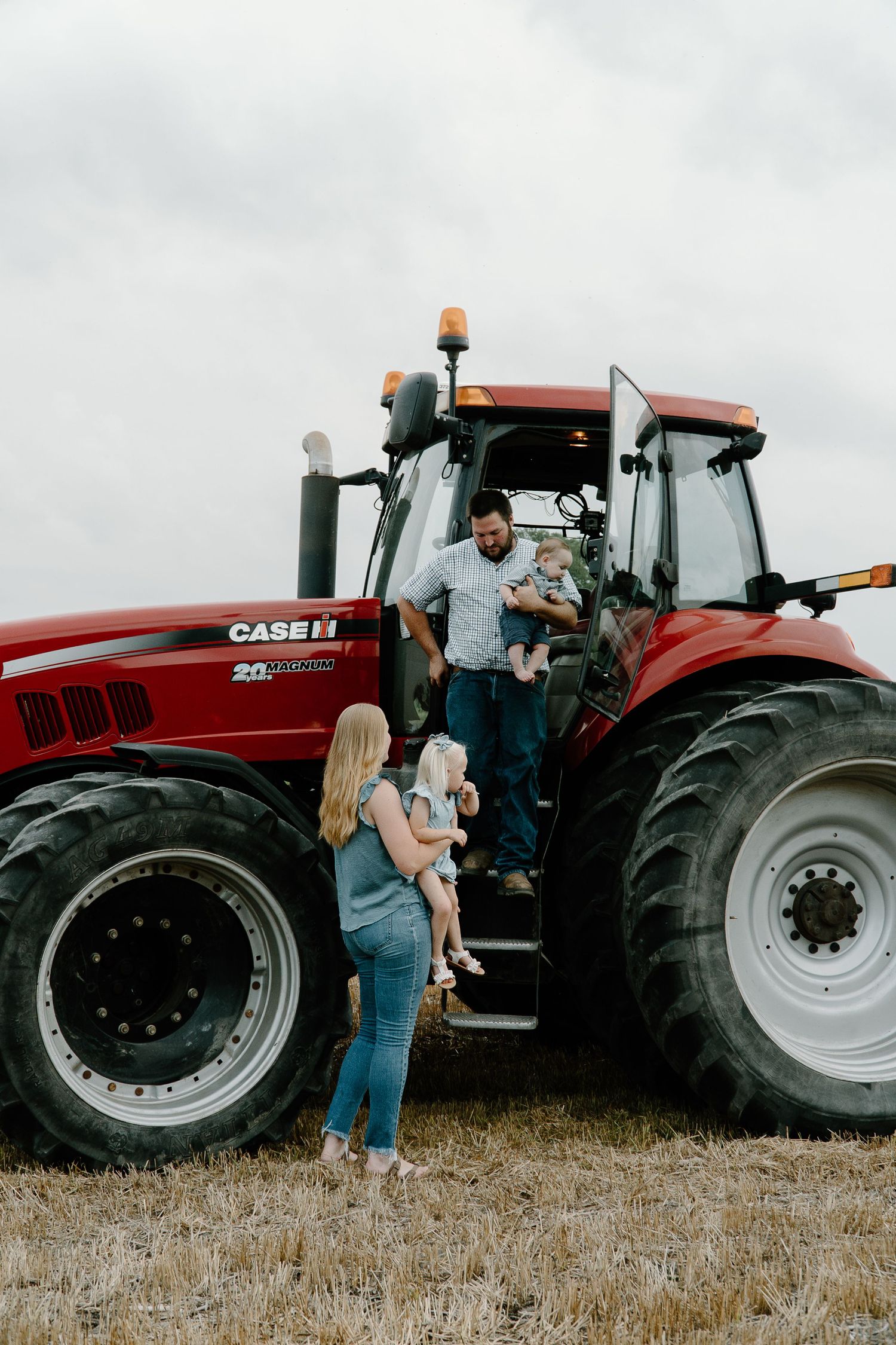 Family with young children posing beside a large red Case IH tractor in a harvested field.