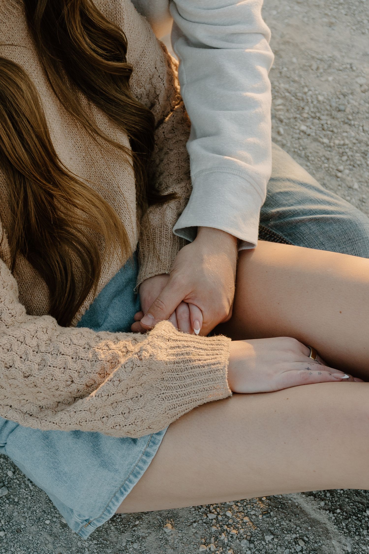 Close-up of a couple holding hands while sitting together on sandy ground outdoors.
