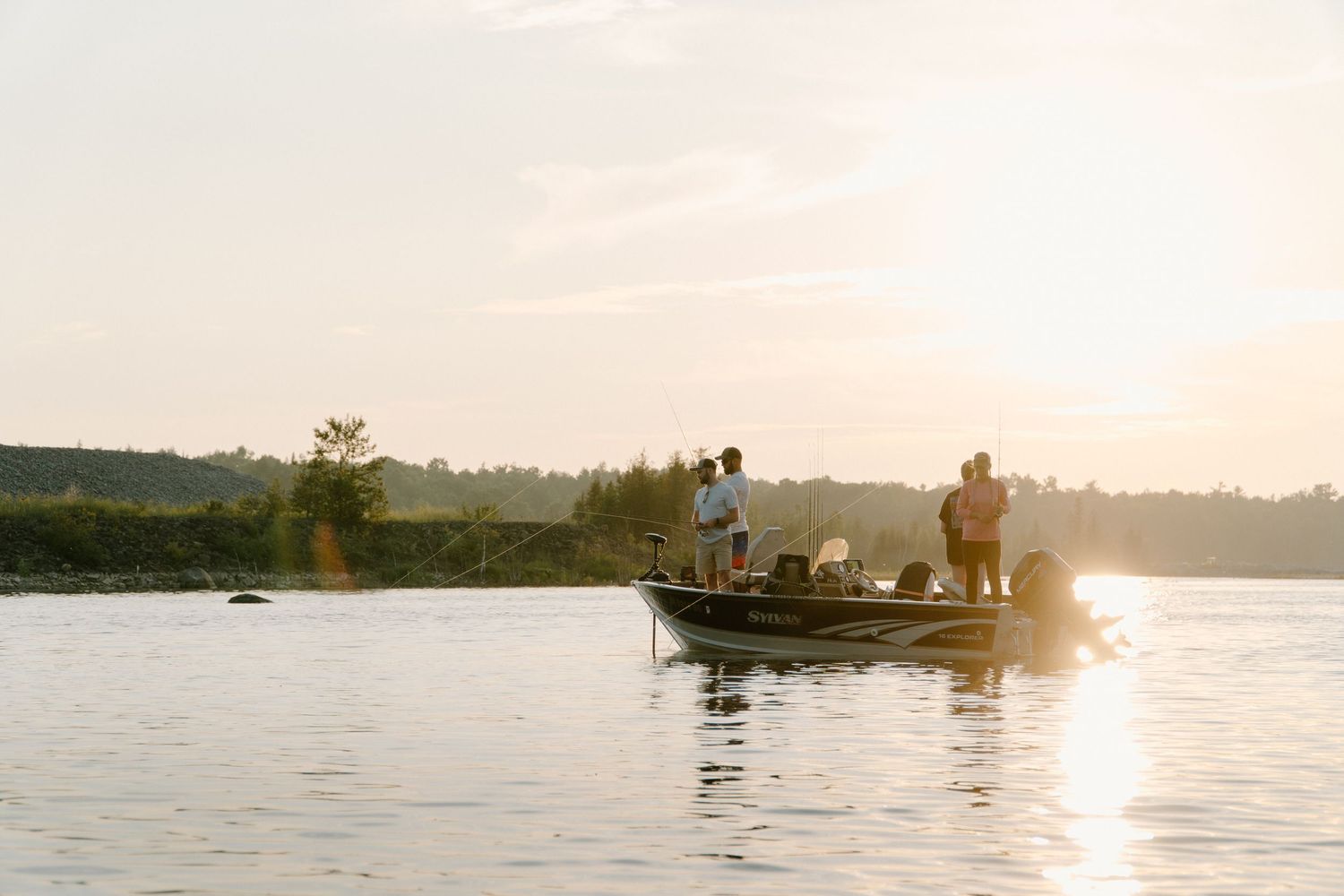 Group of people fishing from a motorboat on a calm lake at sunset.