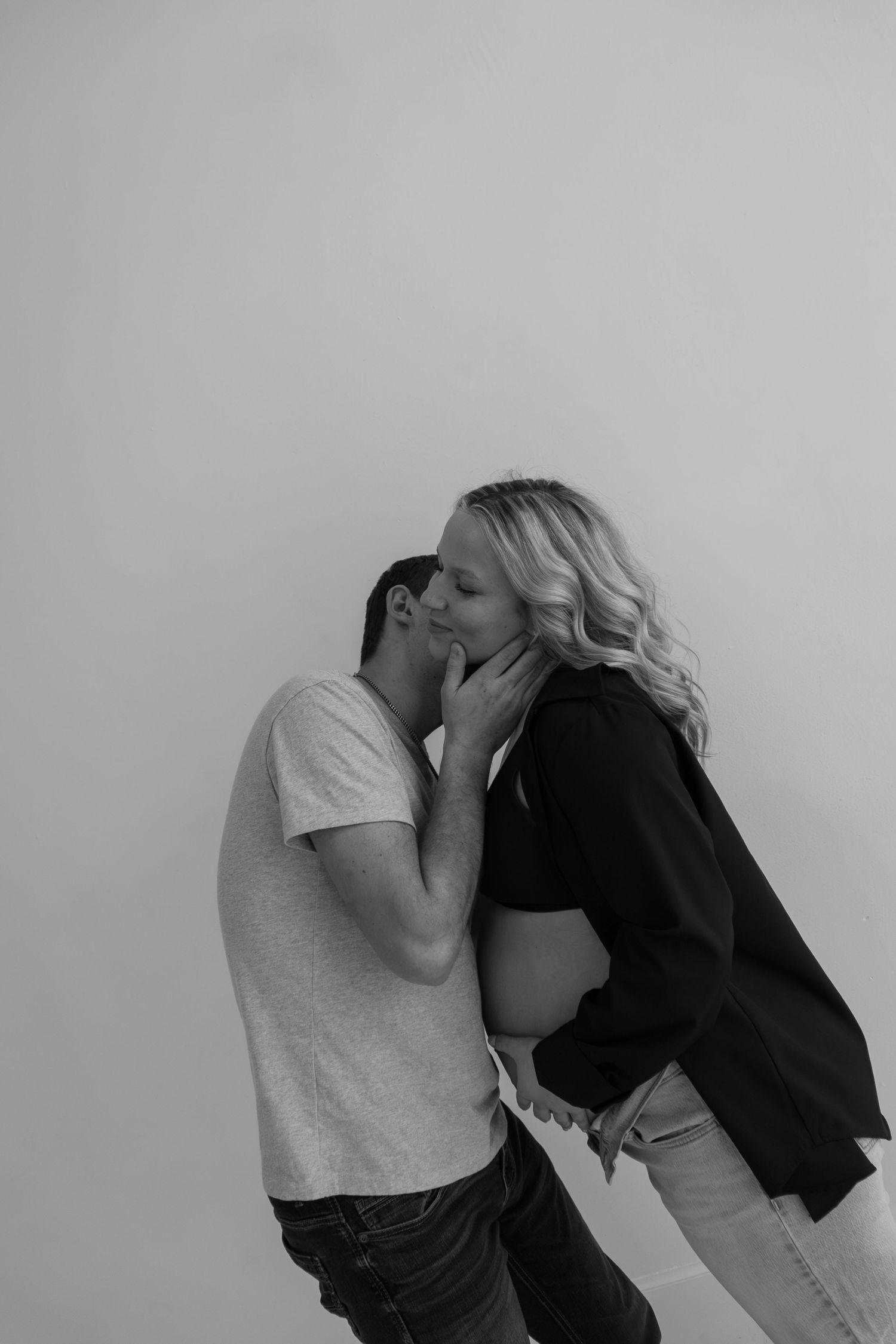 Black and white photo of couple kissing while showing pregnant belly.