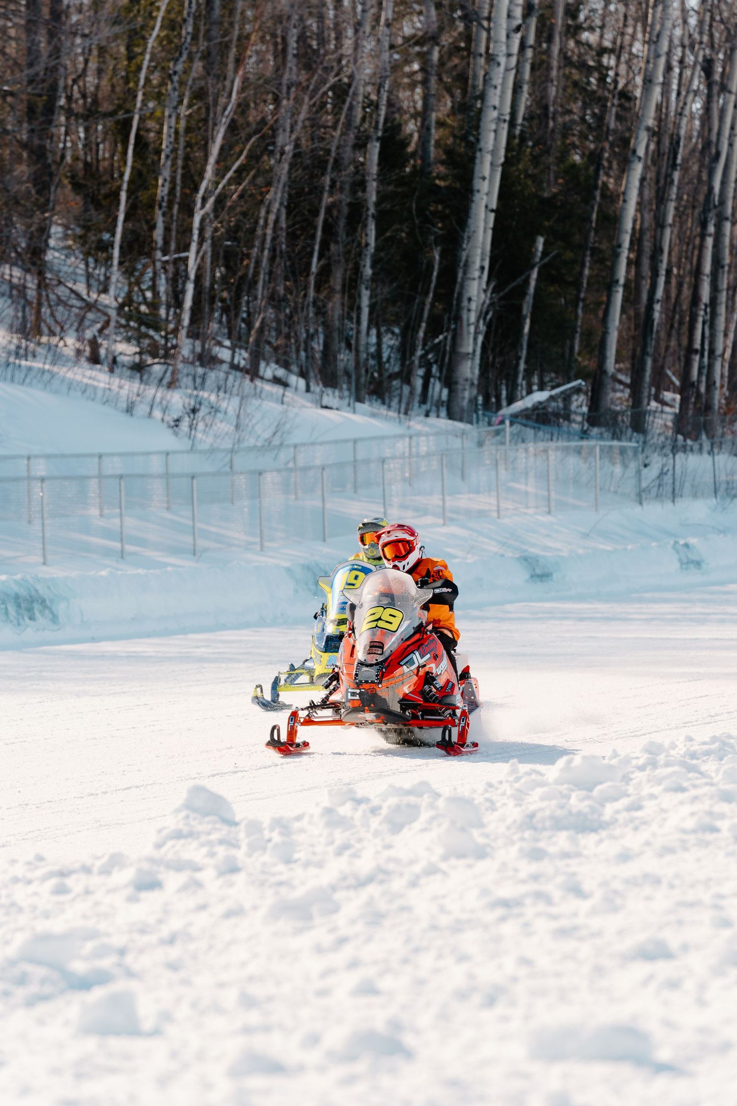 Two snowmobile racers in colorful helmets and gear racing side by side on a snowy winter course.