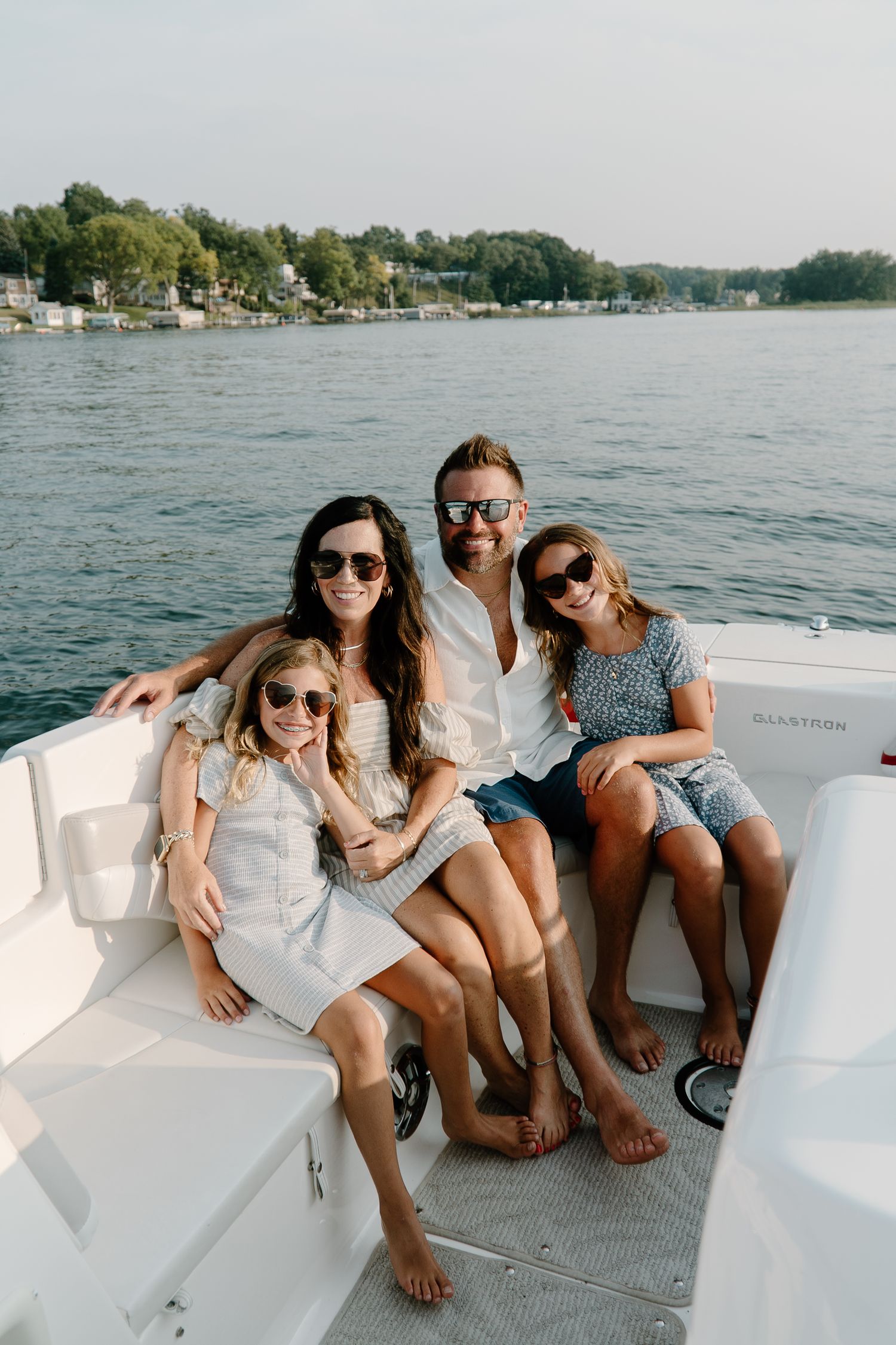 Happy family of four posing on white boat on sunny lake.