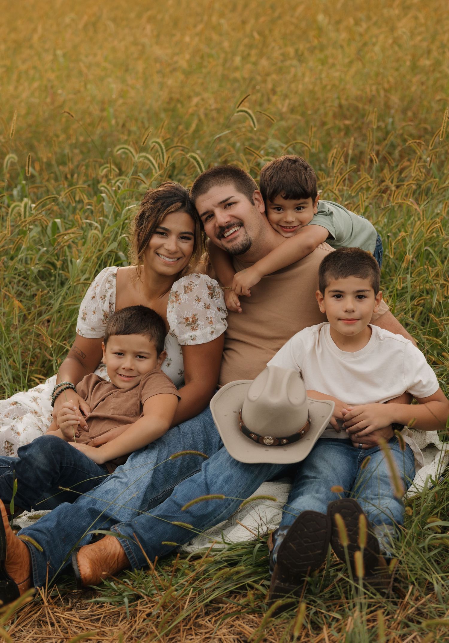 Family cuddles together while sitting in a golden field during sunset.