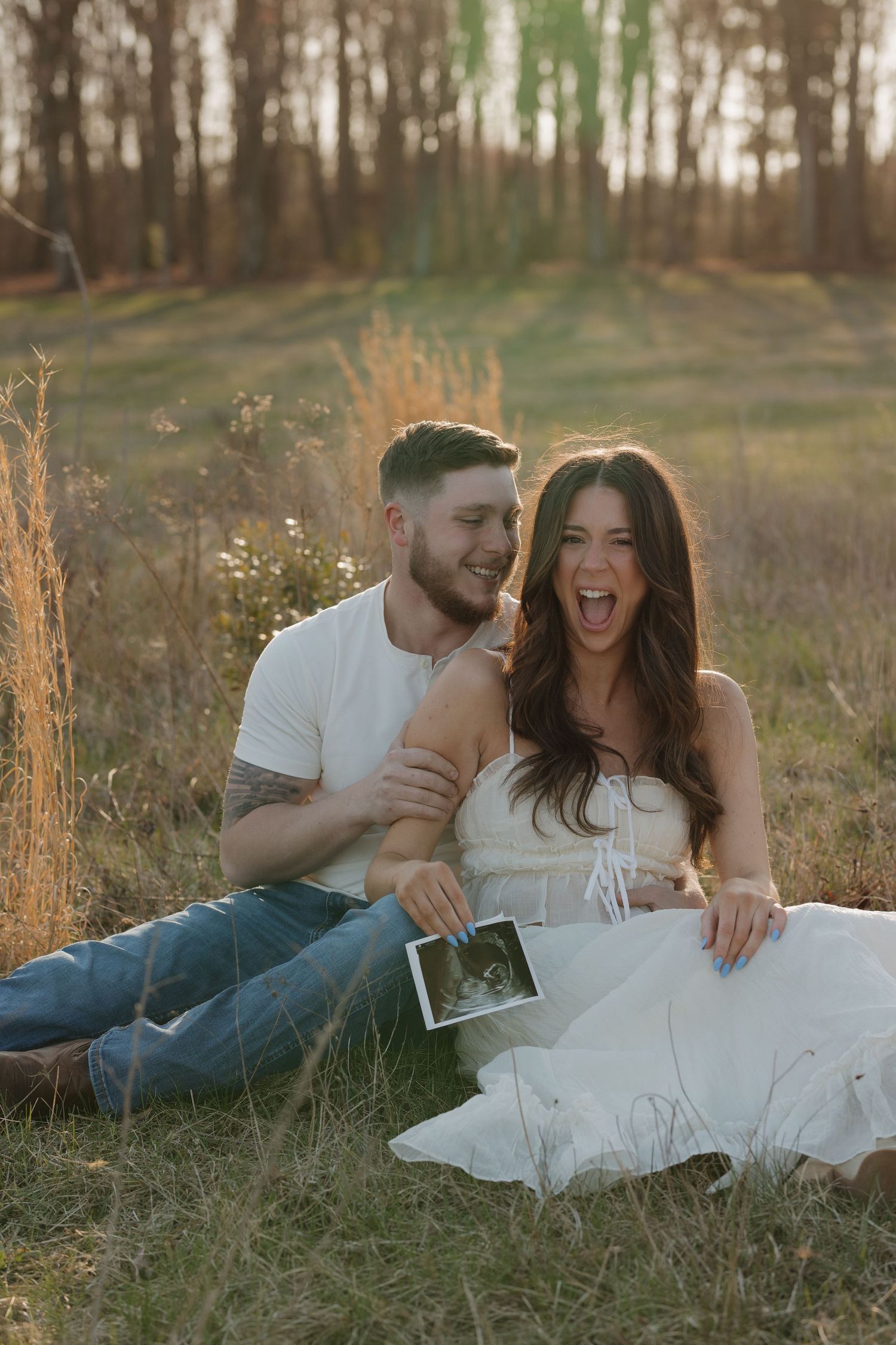 A couple laughing together while lying in grass during a sunset photoshoot.