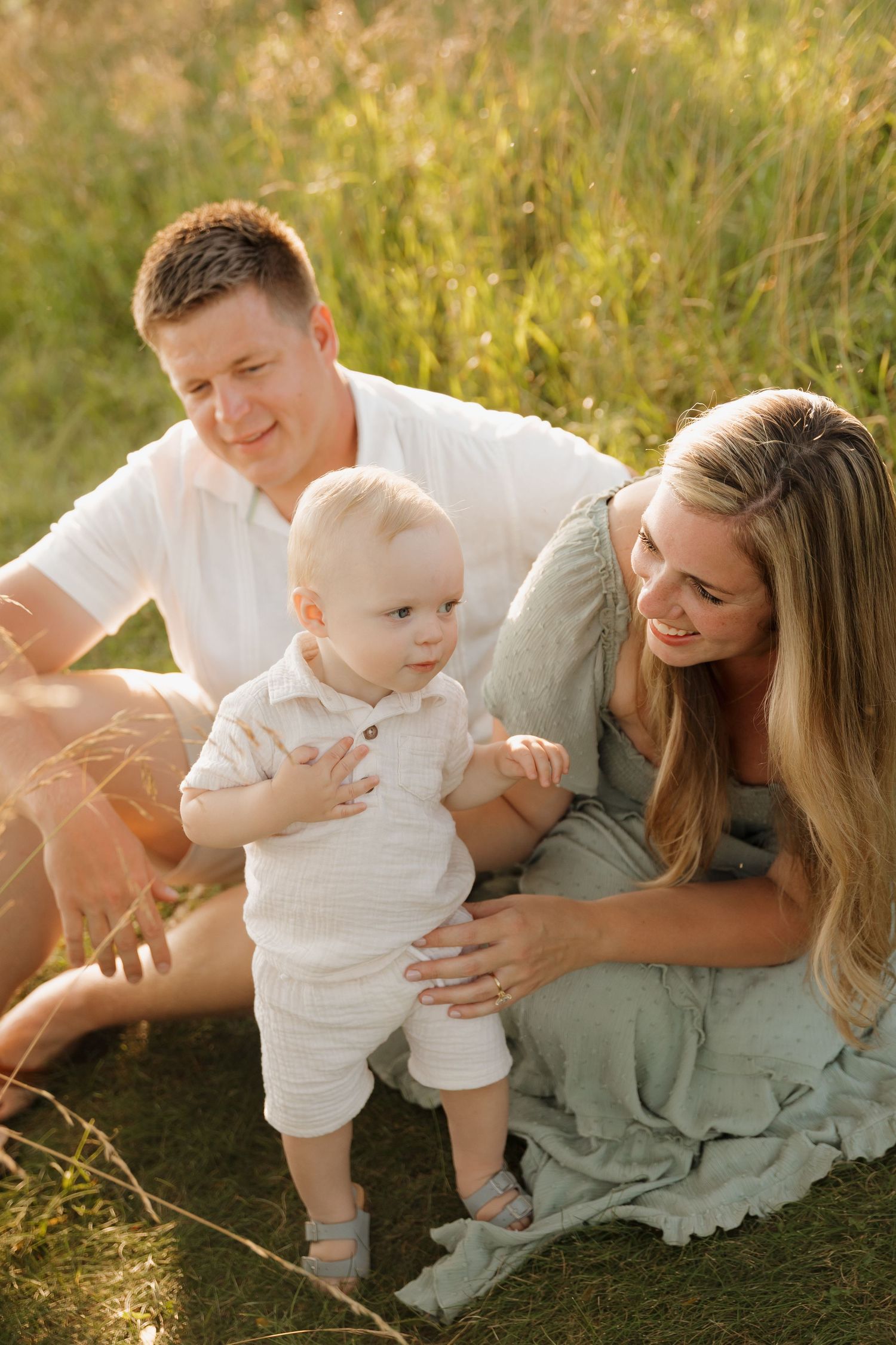Family lying together in a sunlit grassy meadow during sunset.