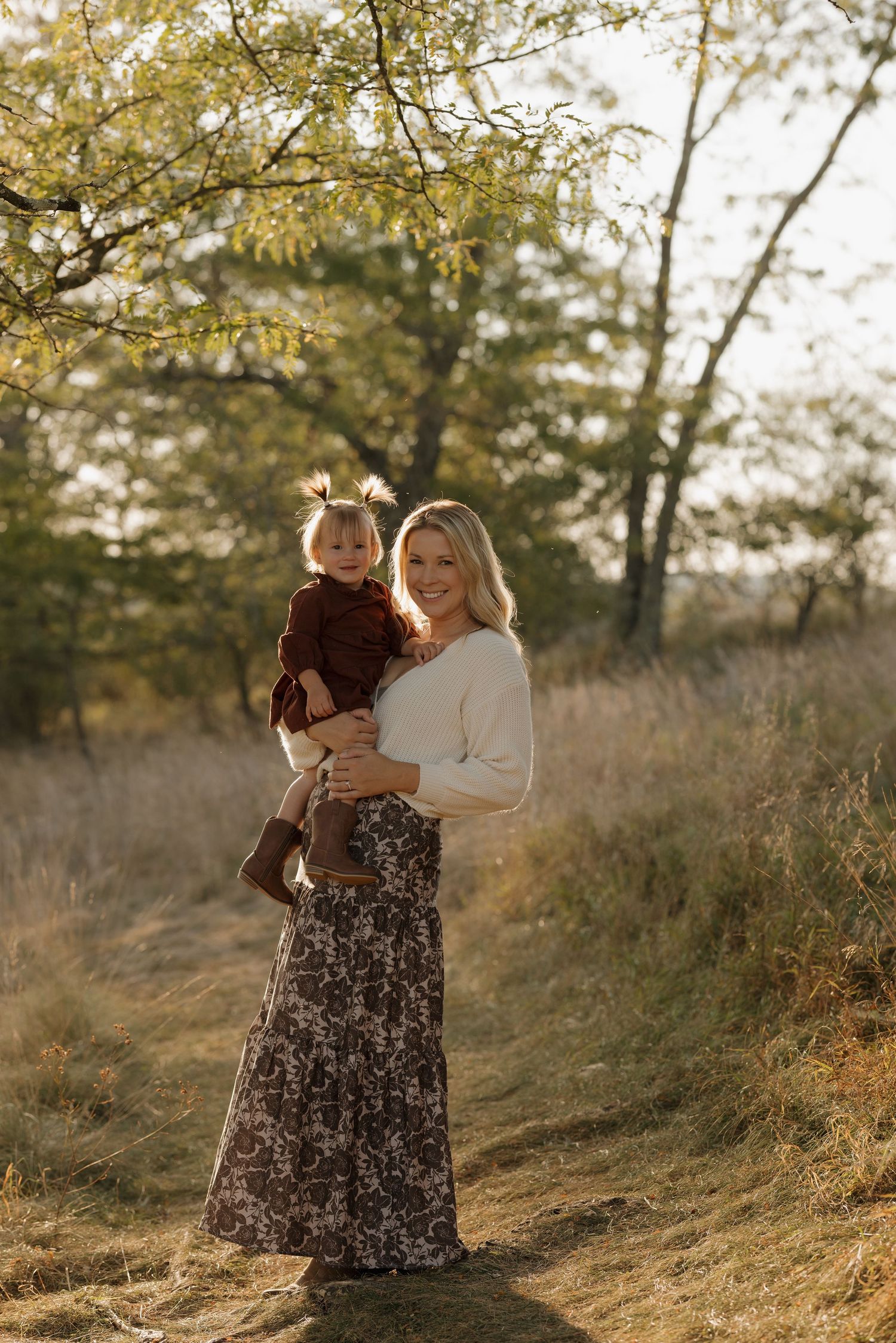 Two people embrace in a sunlit field with autumn trees in the background.