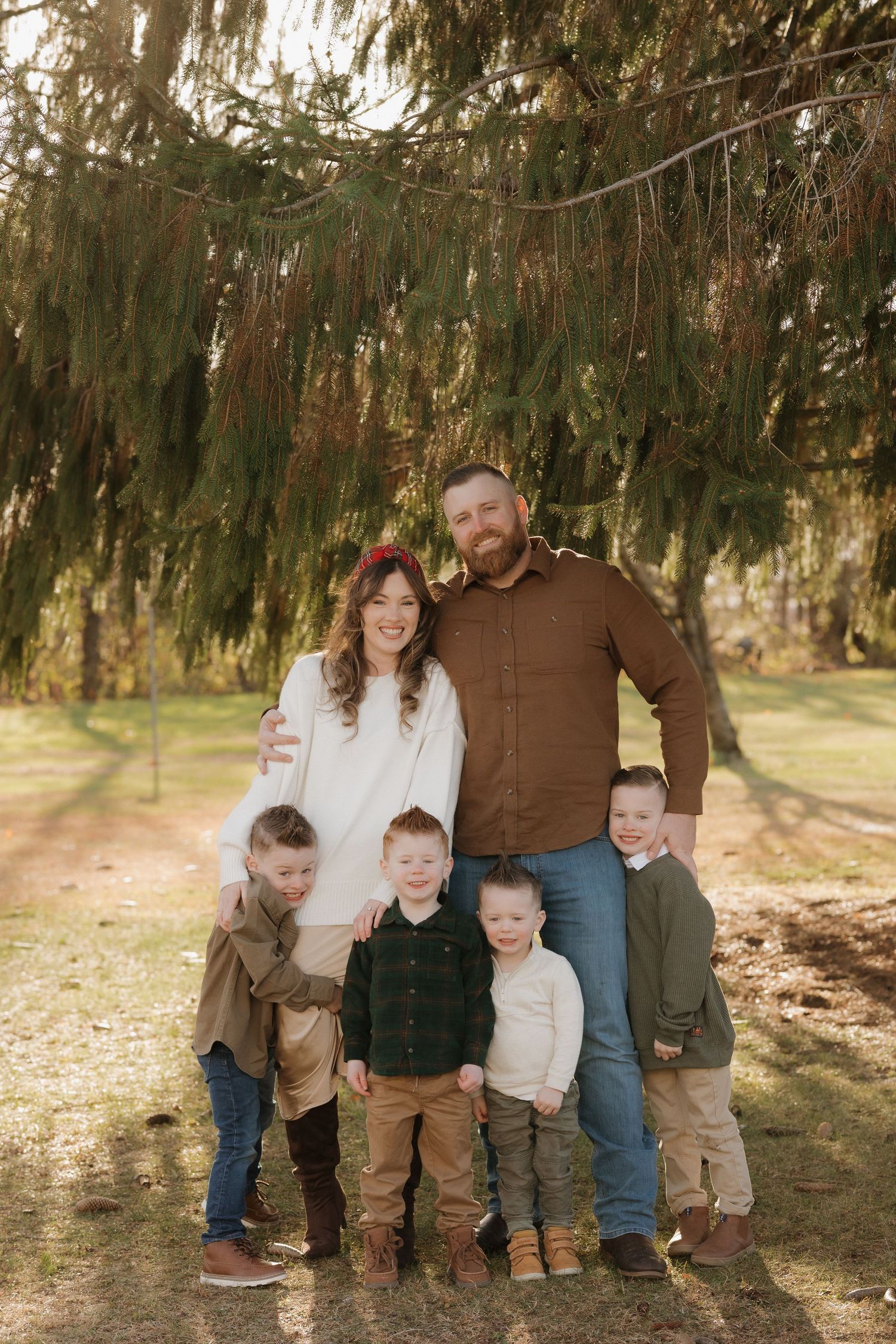 Family group sitting together on ground under evergreen trees.
