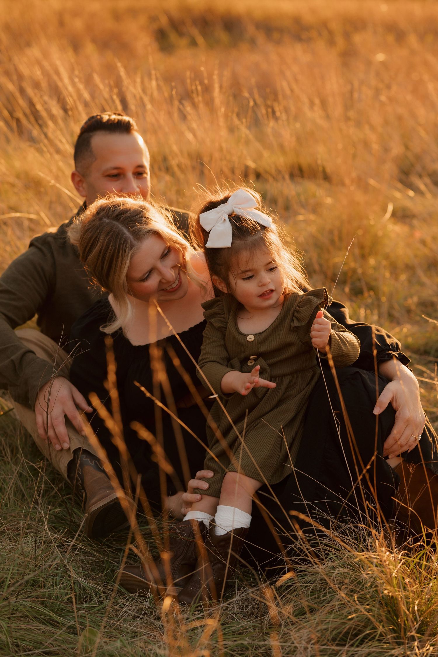 A family shares a tender moment together in a golden field at sunset.