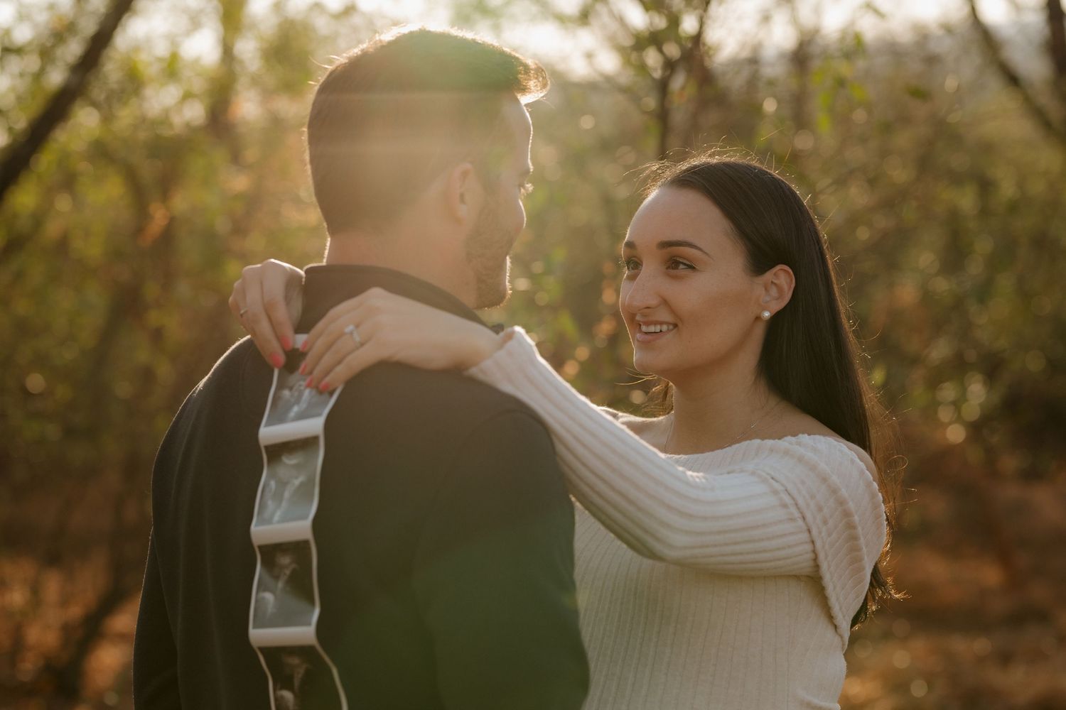 A couple in casual attire embraces while sharing a tender moment outdoors.