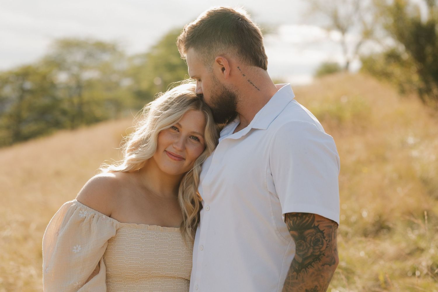 A couple shares intimate moments in a golden field during sunset while wearing casual attire.