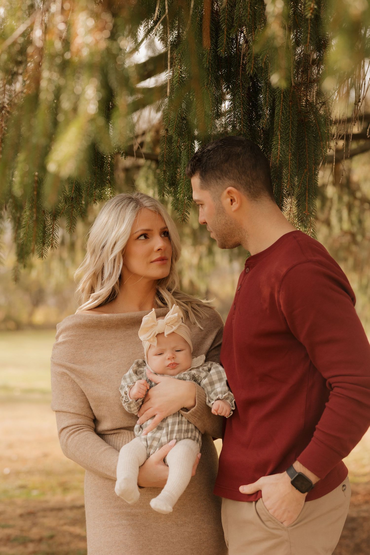 Family in coordinating autumn colors poses together under evergreen branches during outdoor photo session.