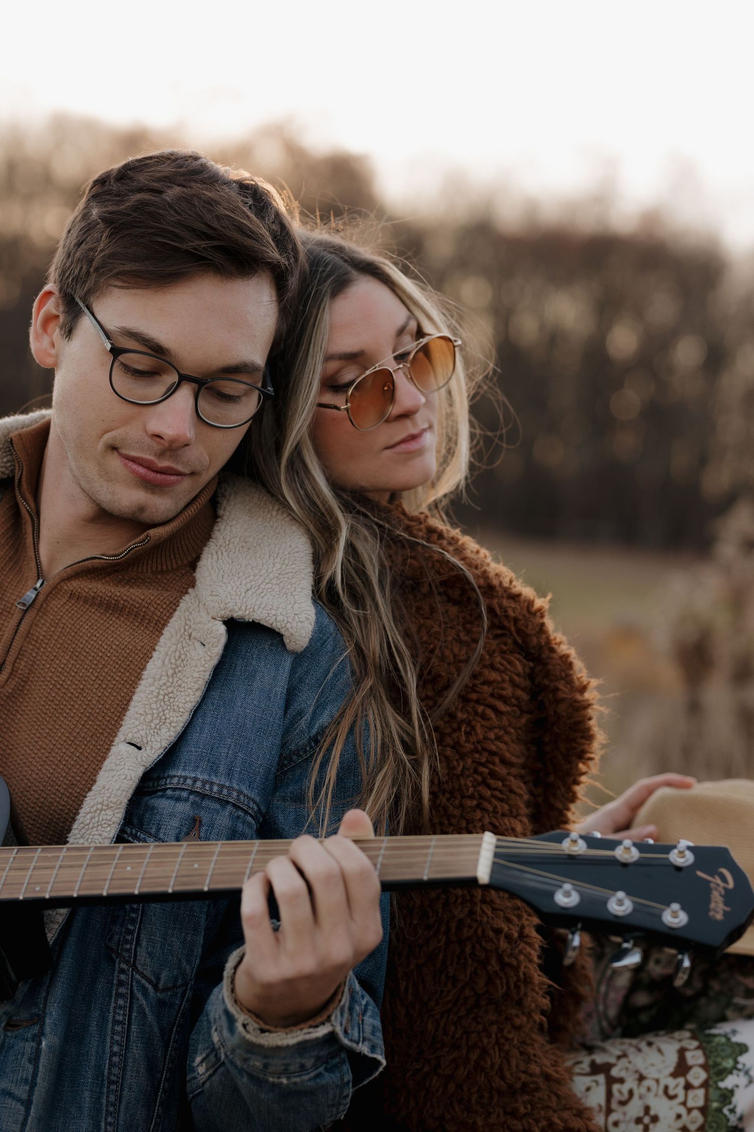 Couple sharing an intimate moment while playing acoustic guitar at sunset in a rustic outdoor setting.