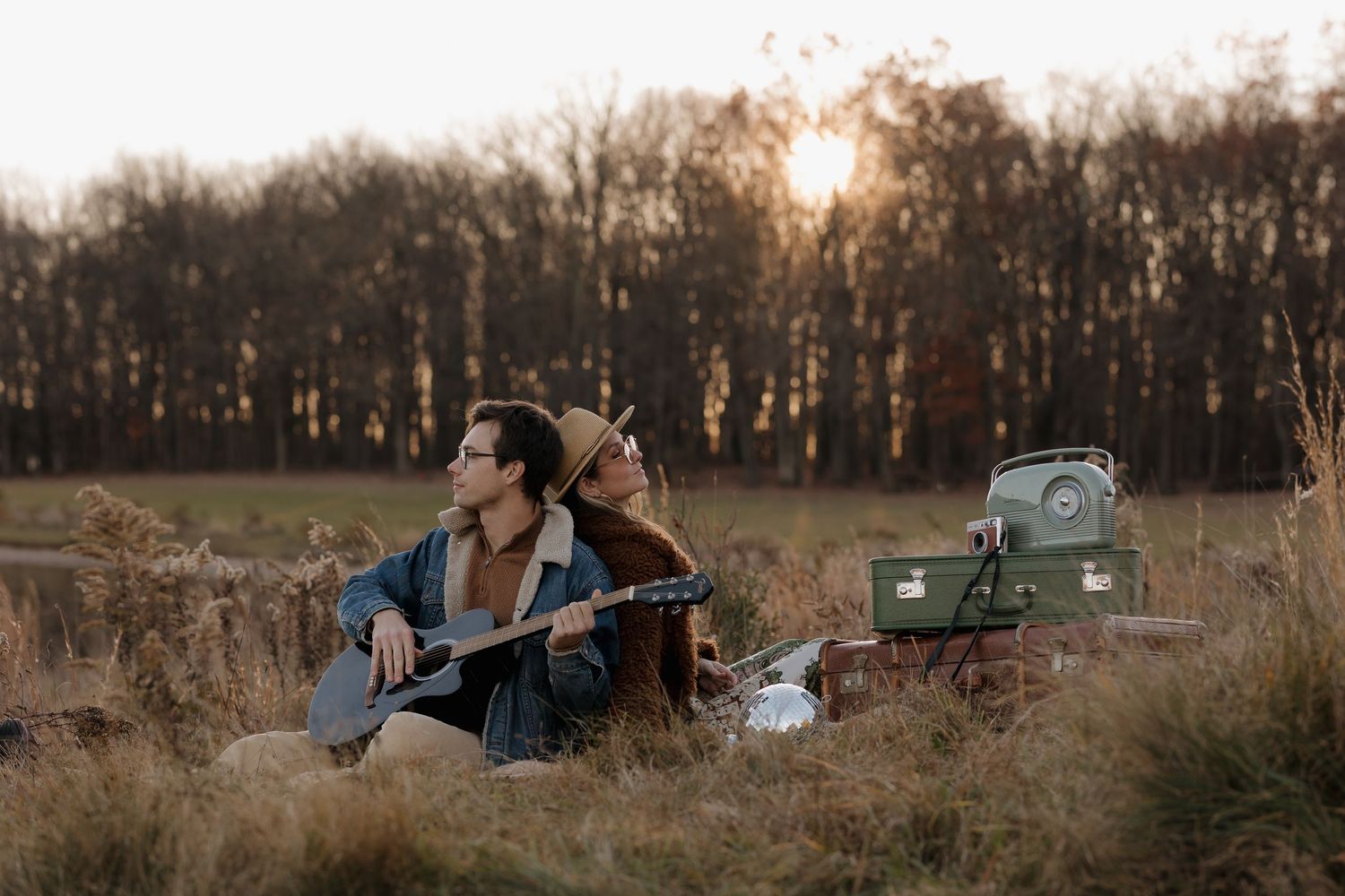 Couple embracing in winter coats against a sunset backdrop with vintage cars in background.