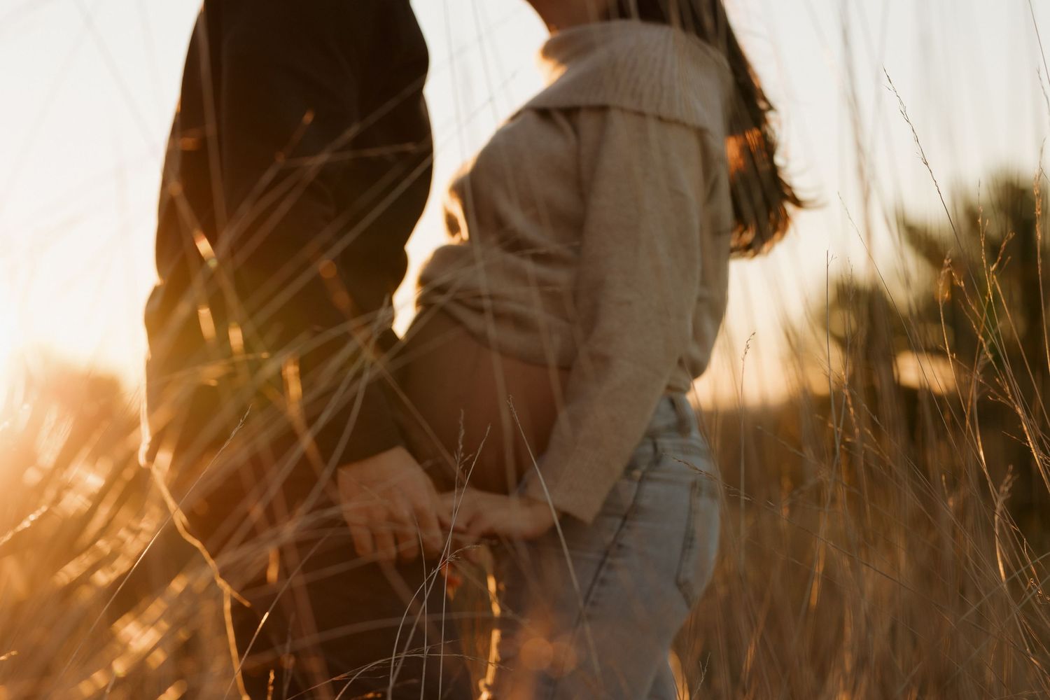 Couple embracing in a golden field during sunset creating a romantic silhouette against the warm sky.