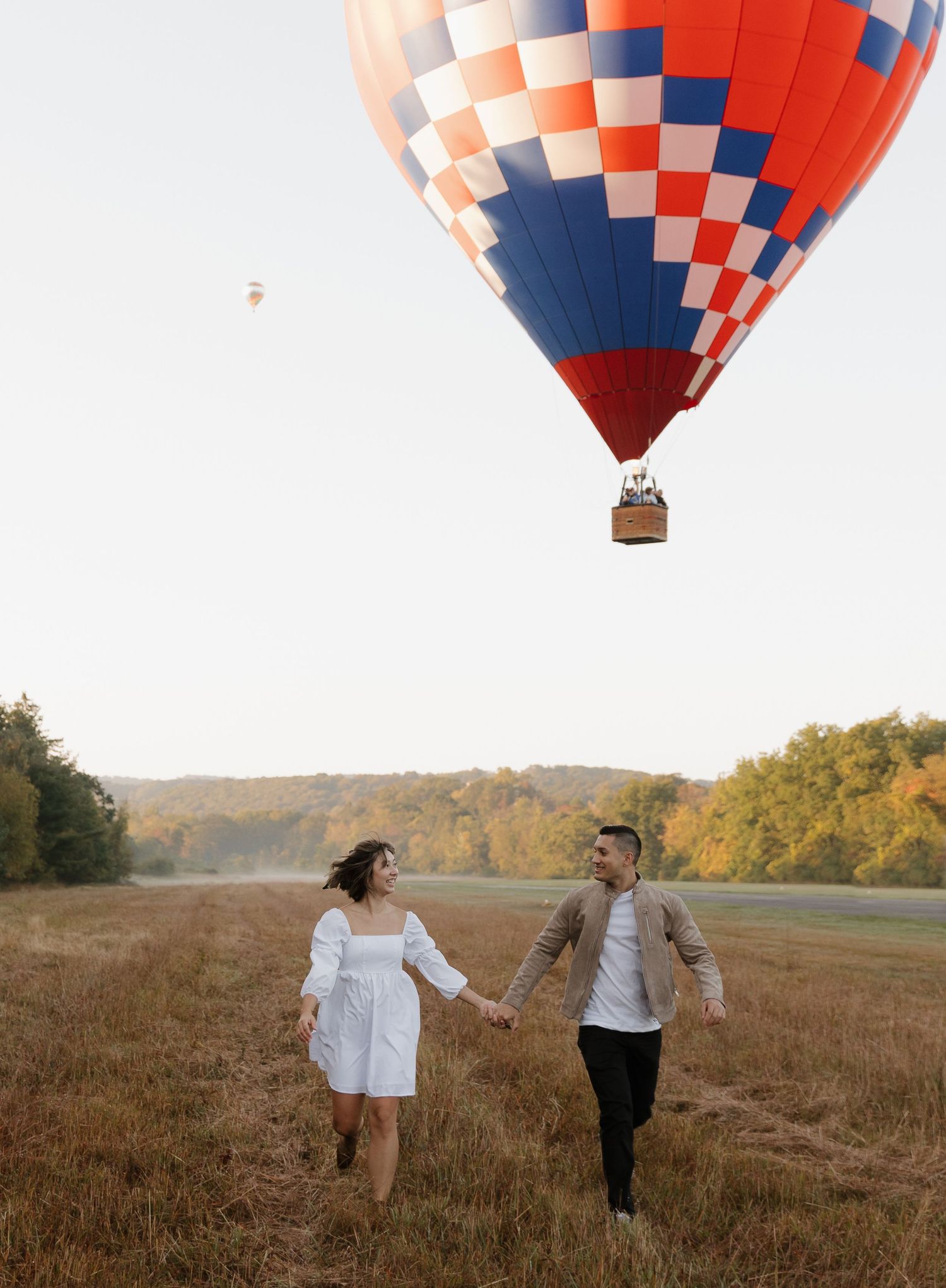 Red and blue hot air balloon floating above a rustic field at sunset.