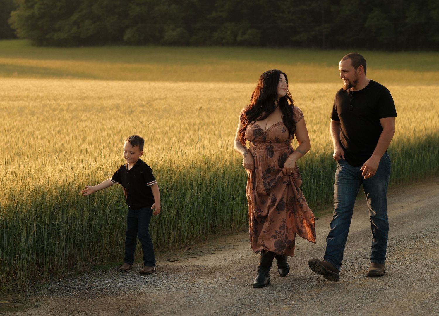 A family walks together along a path through a golden wheat field at dusk.