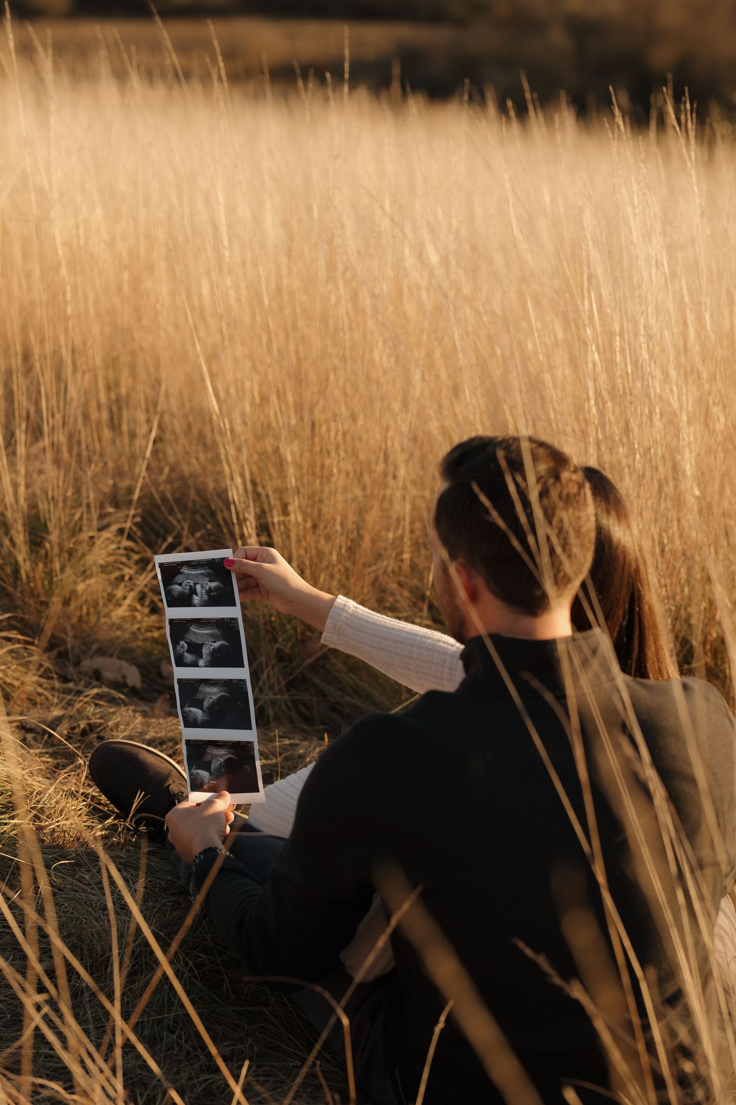 Two people looking at ultrasound photos while sitting in tall grass at sunset.