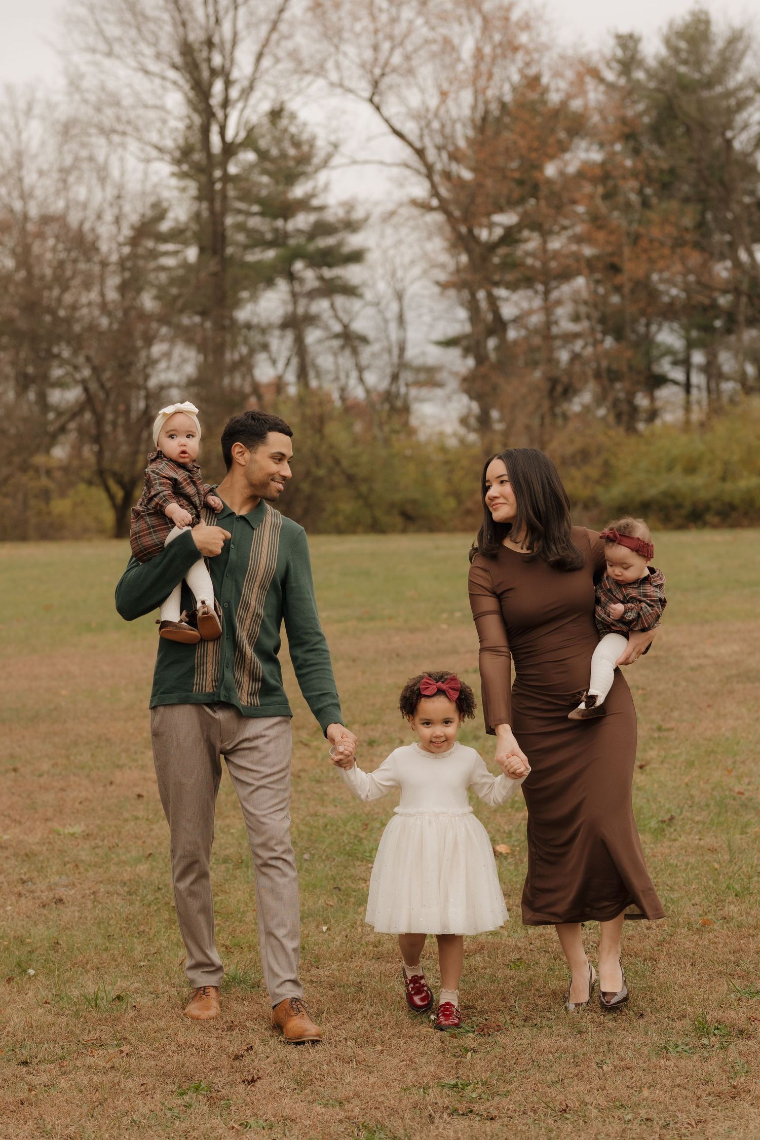 A family walks together on a fall day wearing coordinated brown outfits in a grassy field.