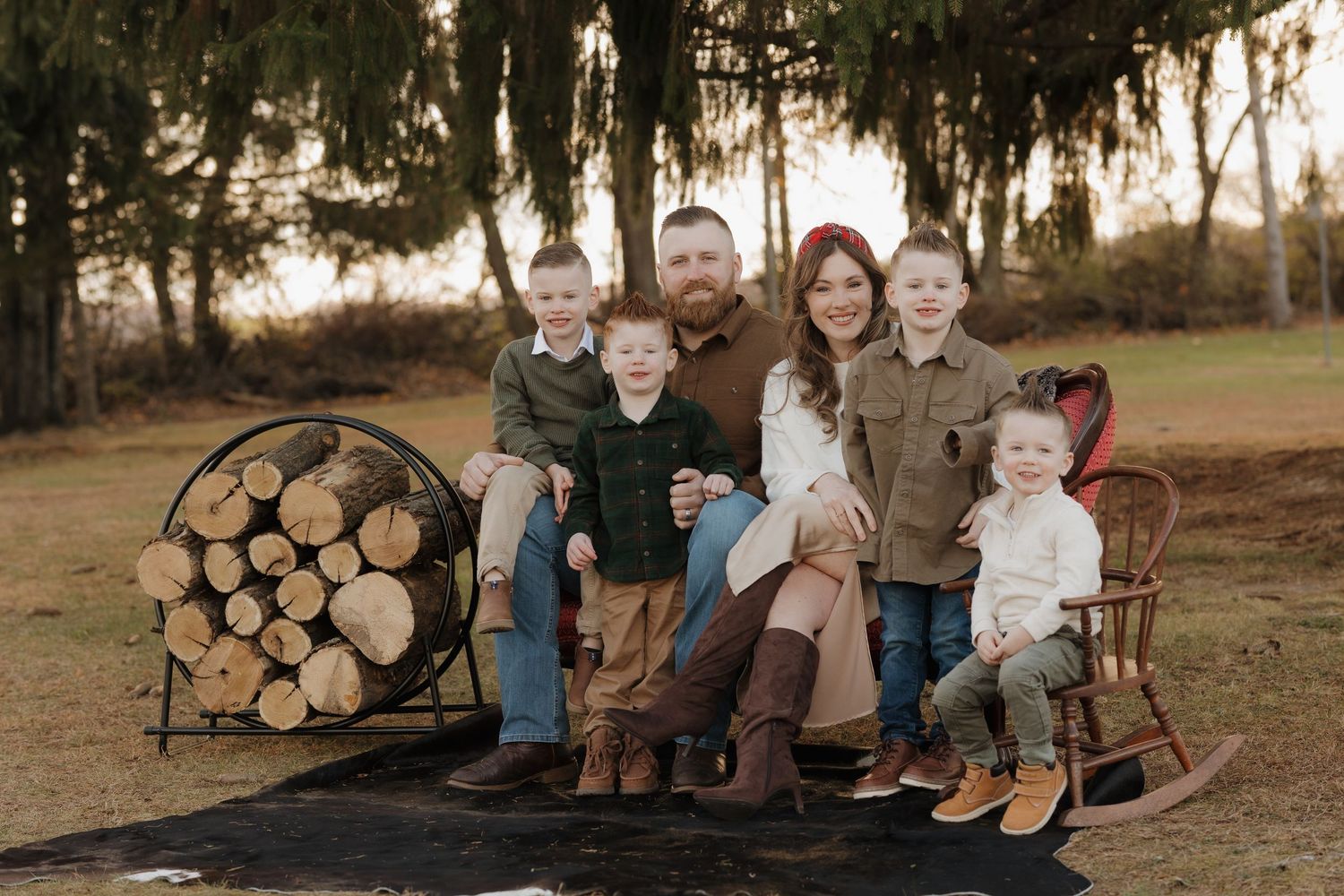 Family gathering for a casual outdoor photo session near stacked firewood.